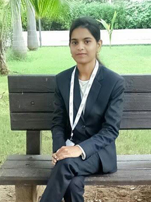 A young woman sits on a bench in a green outdoor setting.