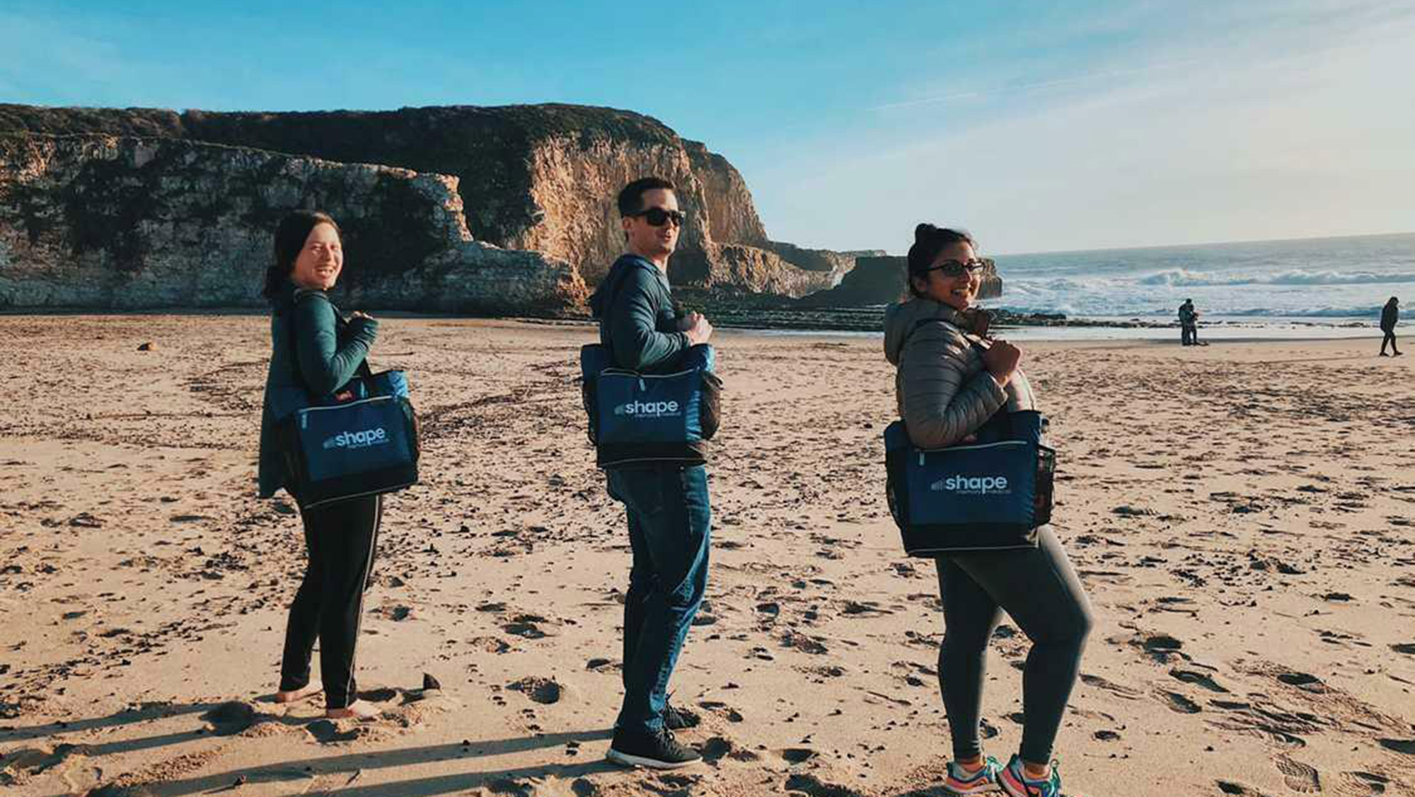 Three people on a beach with Shape Memory Medical bags.