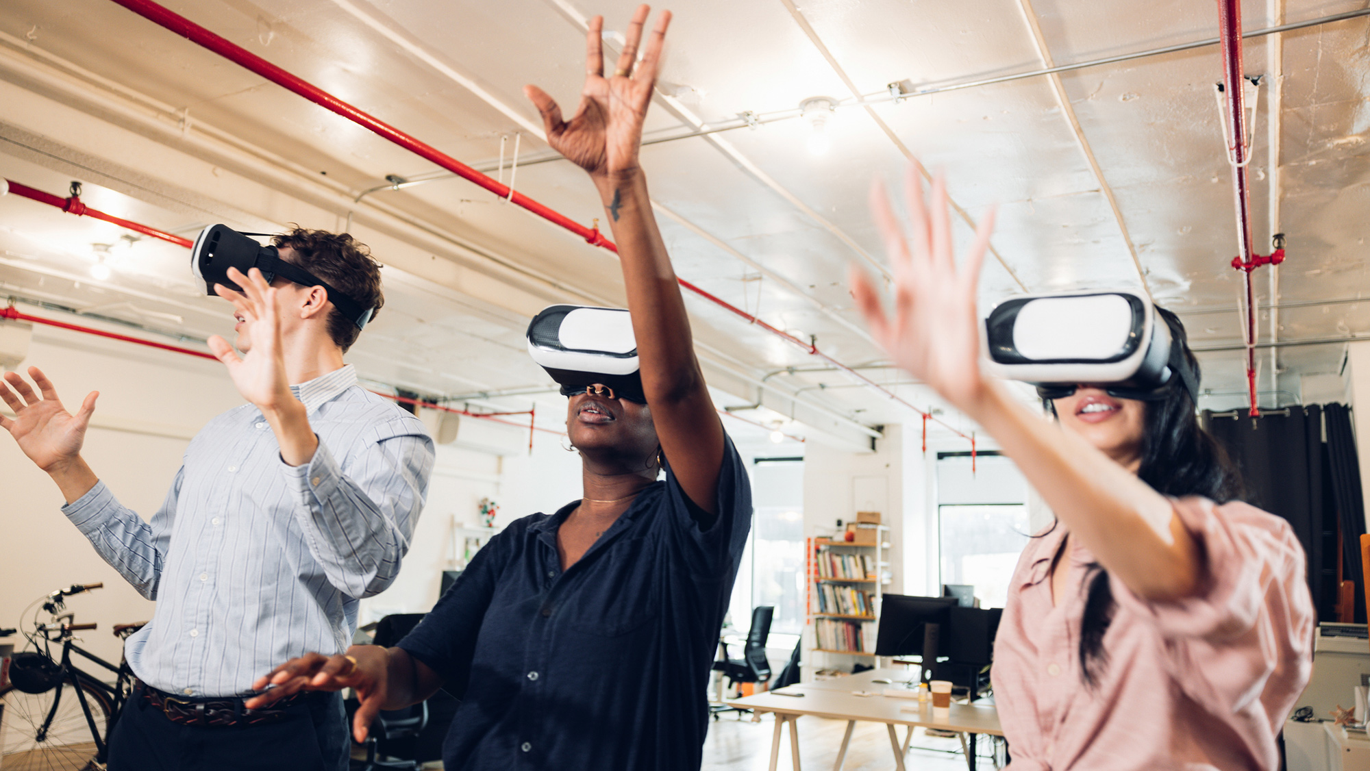 Three students wearing virtual reality headsets gesture with their hands.