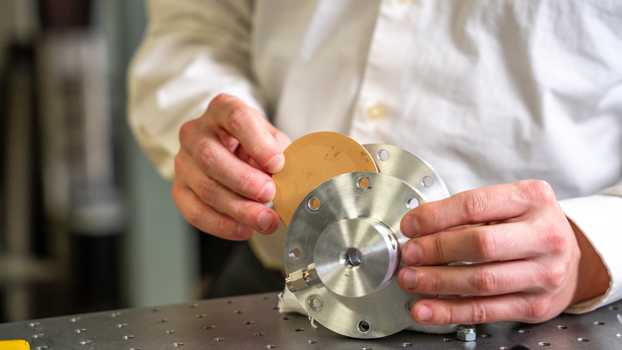 A person wearing a white shirt inserting a tan disc into a metallic device.