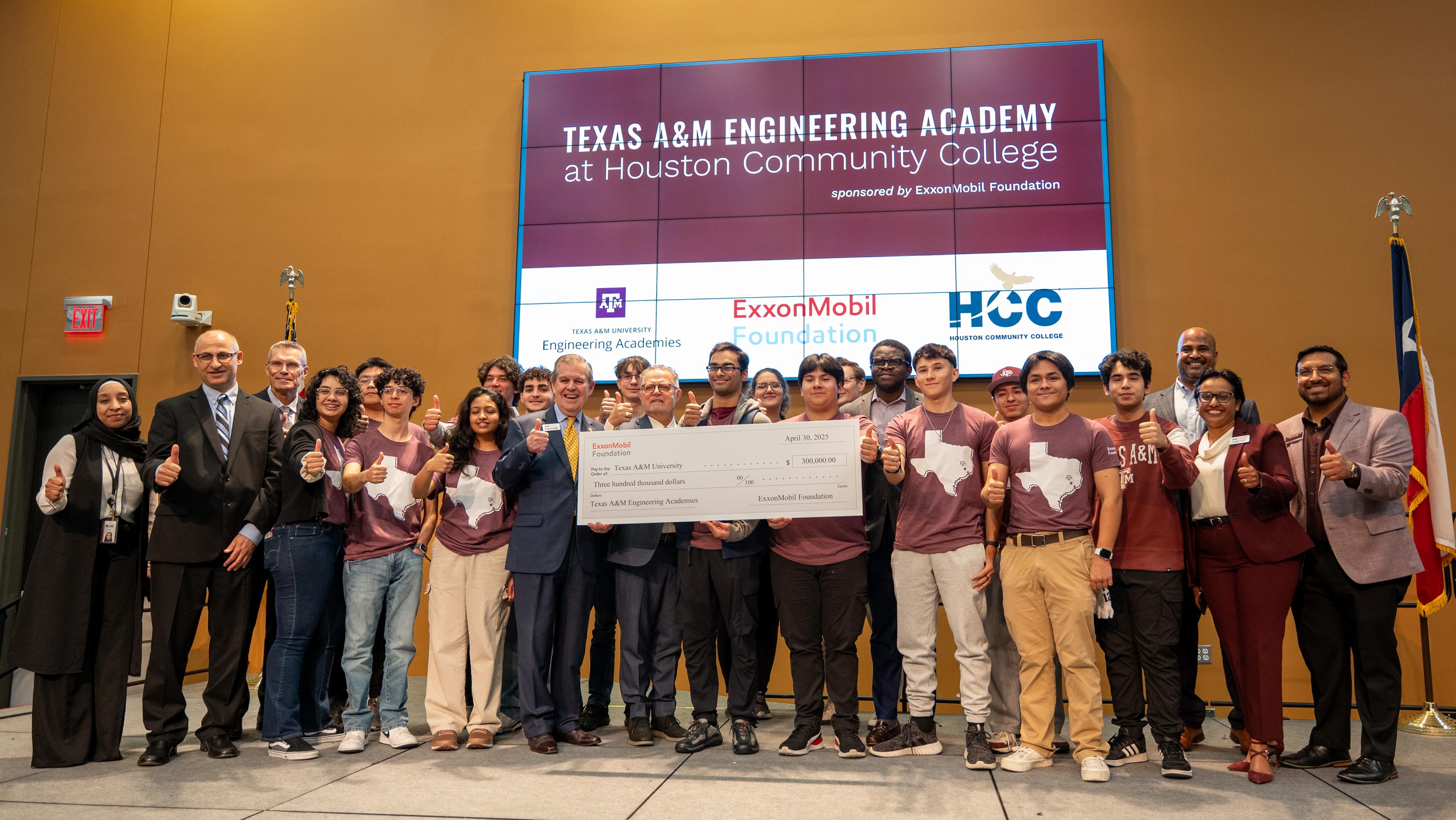 A group of students and academic officials giving a thumbs-up post alongside a ceremonial check.