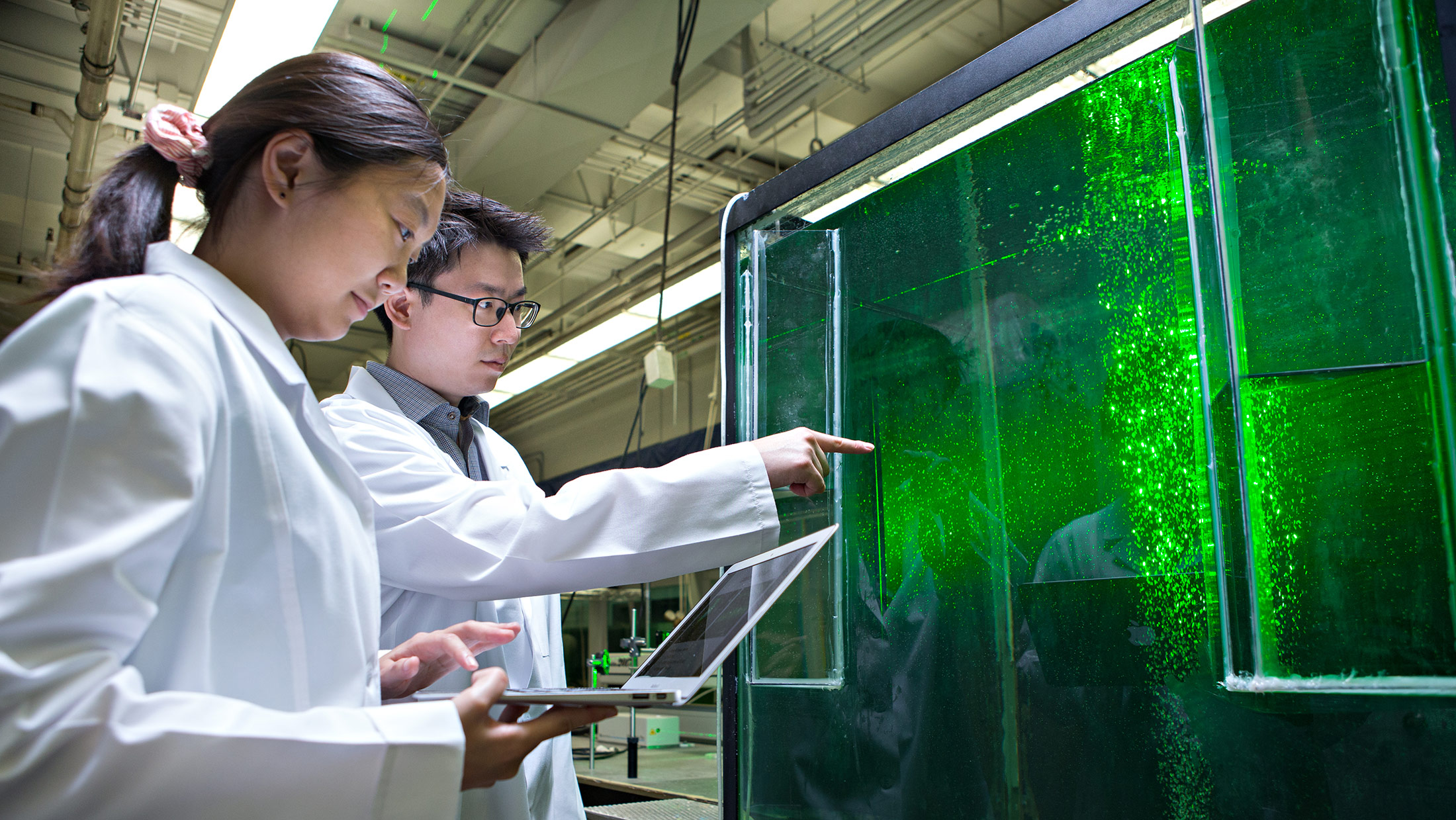 Two people in lab coats studying a water tank in a lab. 