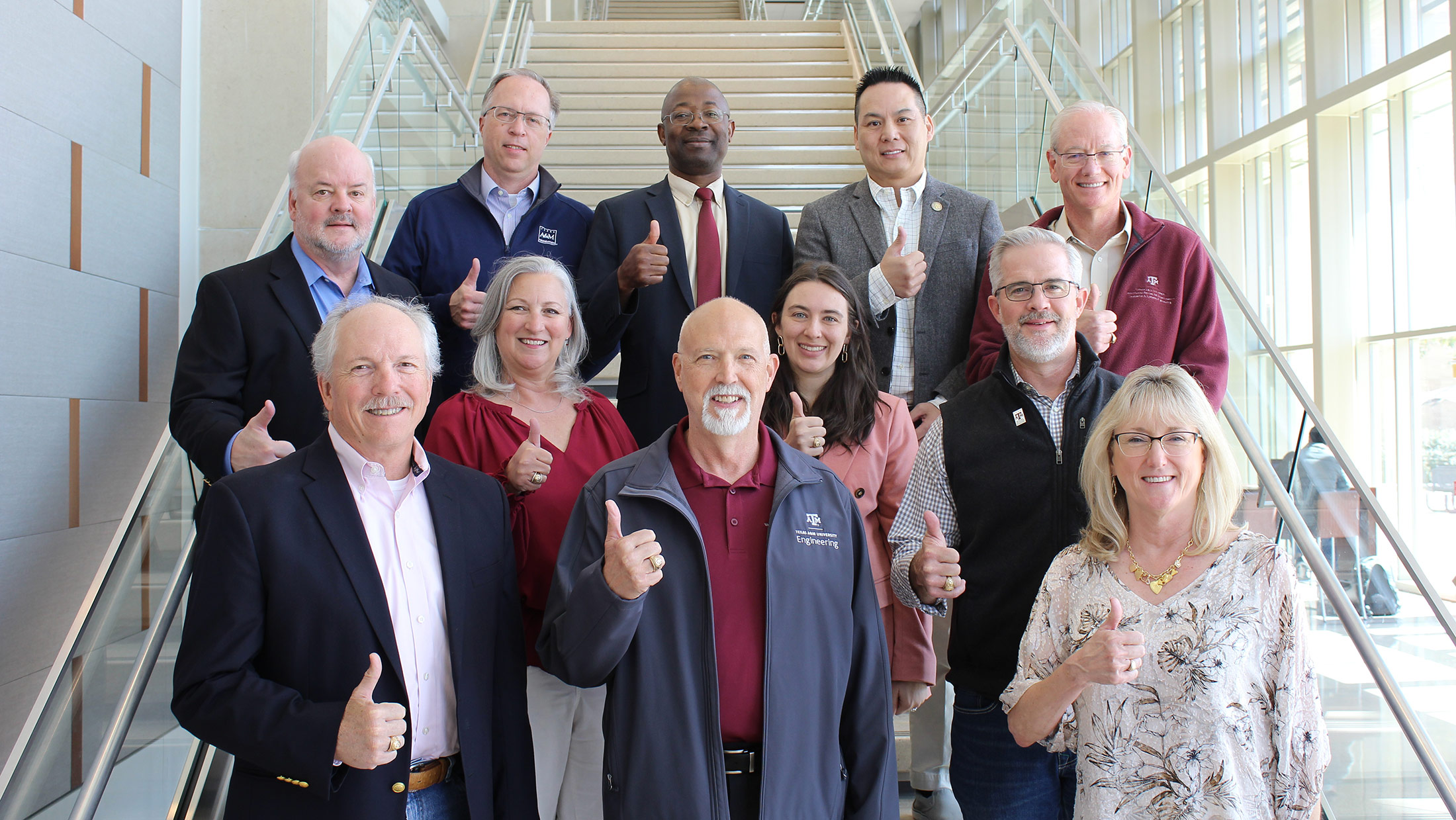 Members of the ISEN Advisory Council standing on a staircase indoors, smiling and flashing a Gig 'Em. 
