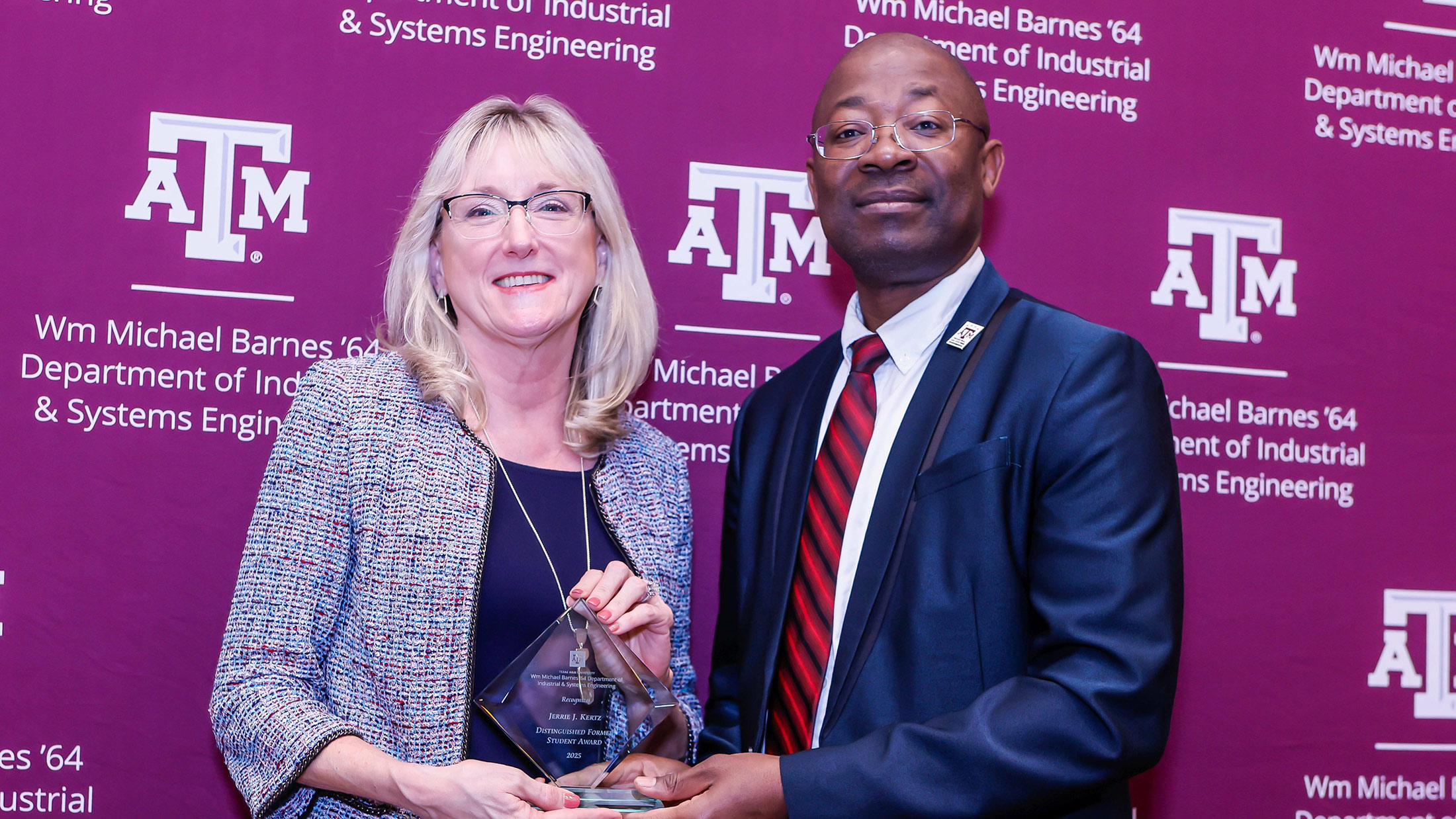  A woman and a man stand in front of a backdrop holding a glass award. 