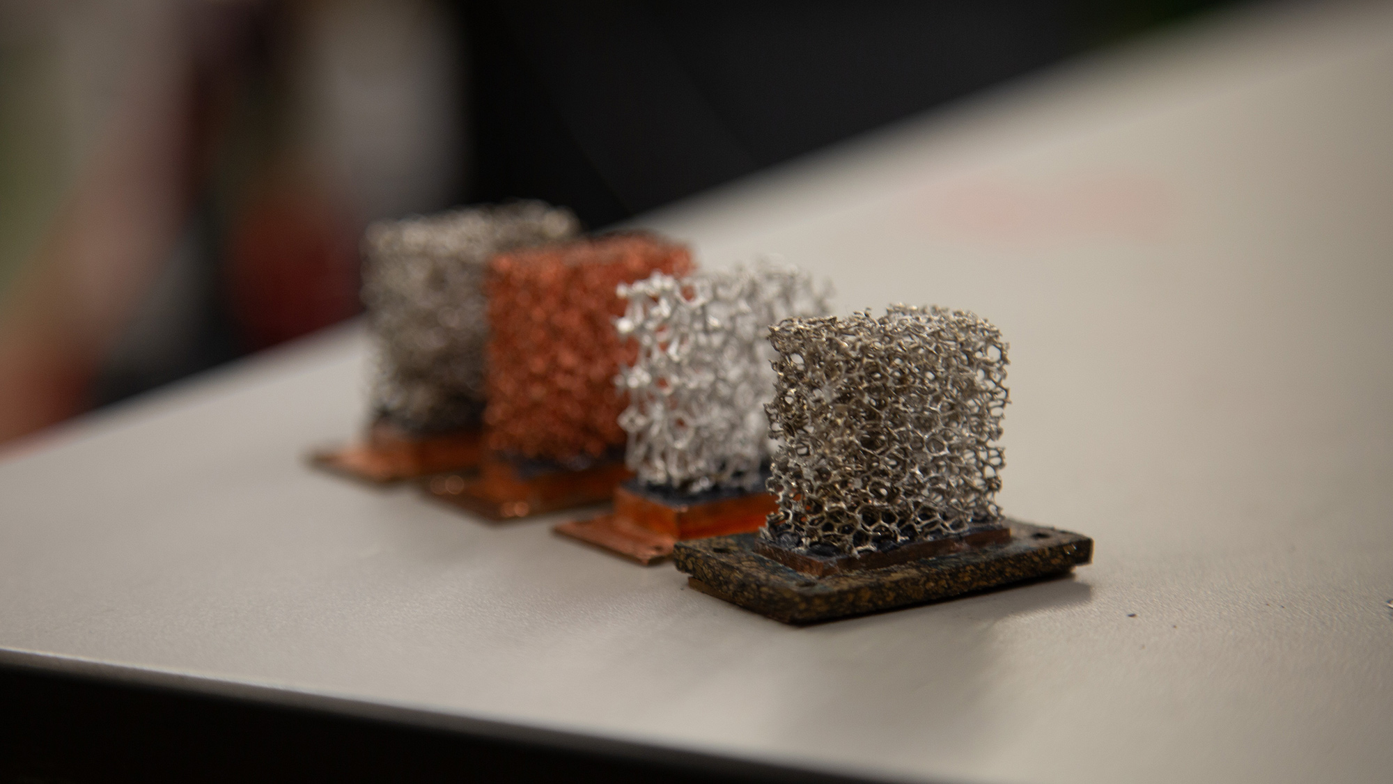 Four small metal structures, each on a base, are arranged in a line on a flat surface.
