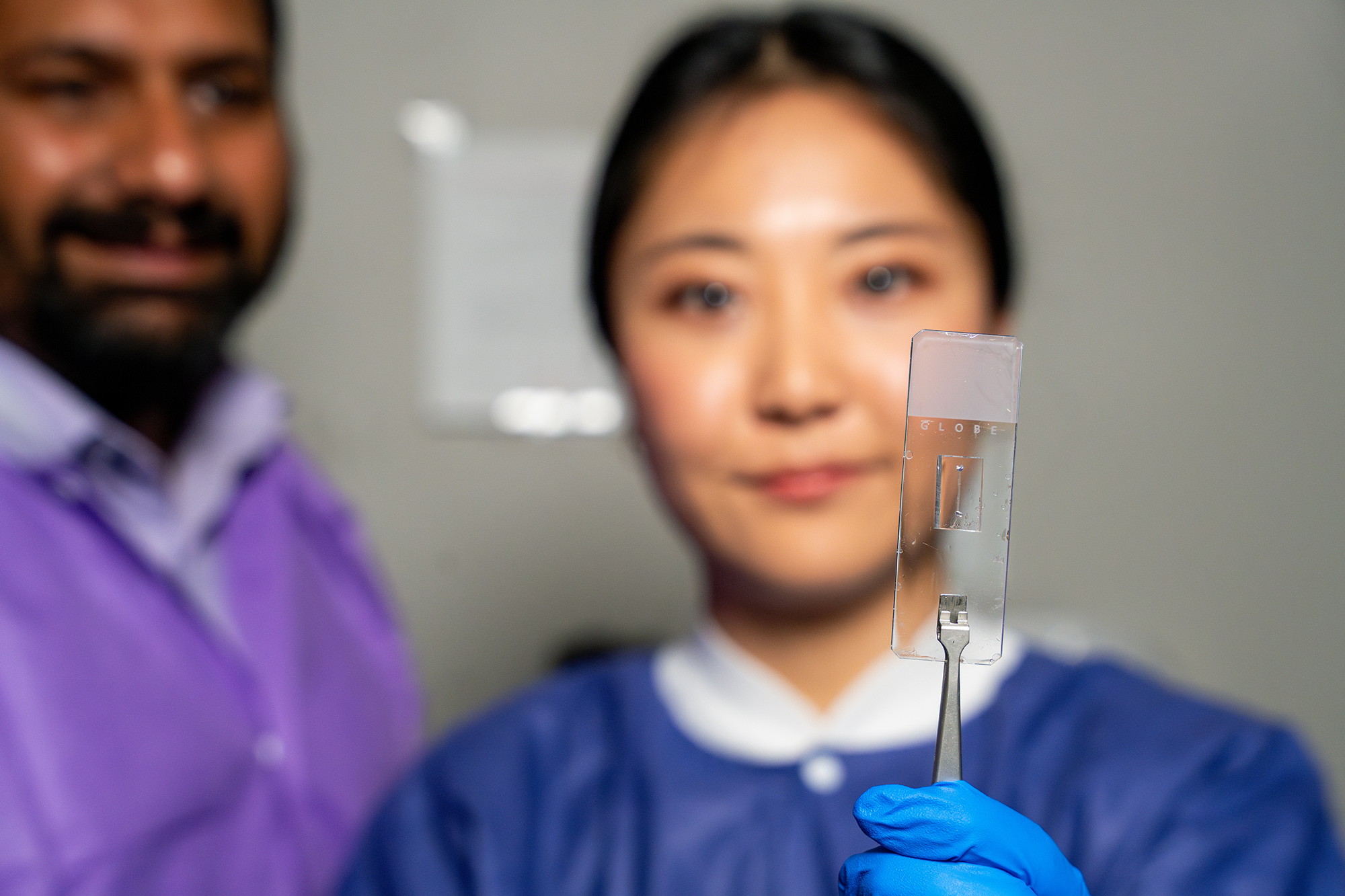 Two researchers looking at a transparent chip held in tweezers.