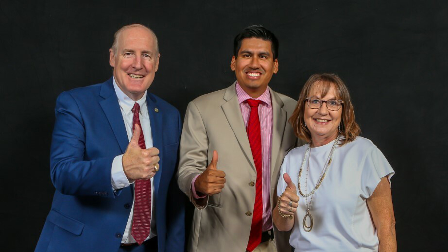Two men and a woman smile and give thumbs up.