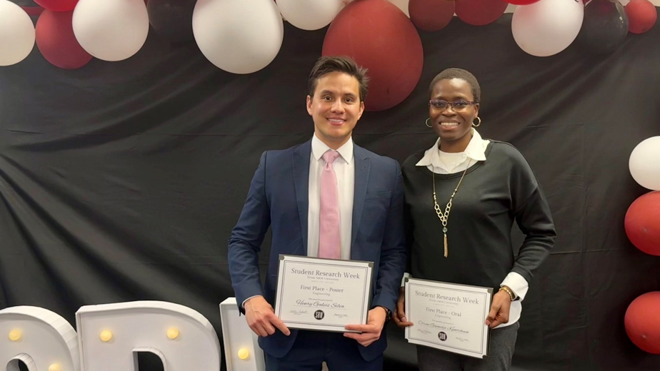 A man and a woman in professional attire stand in front of a black backdrop holding certificates.