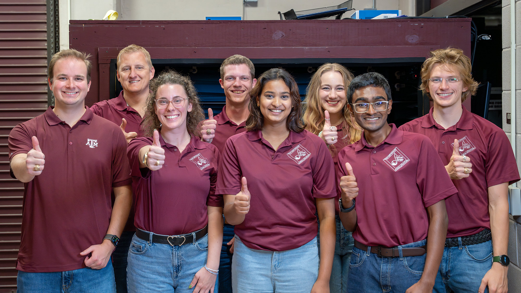 A group of people in maroon shirts giving a thumbs up.
