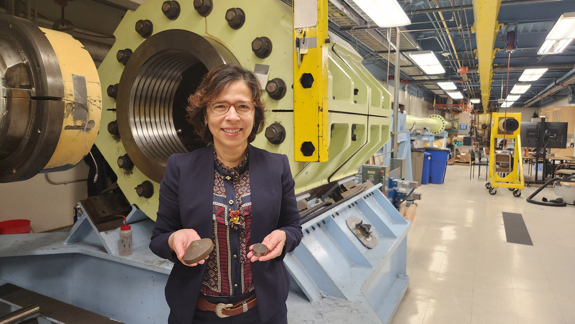 Woman smiling in a lab in front of large equipment.