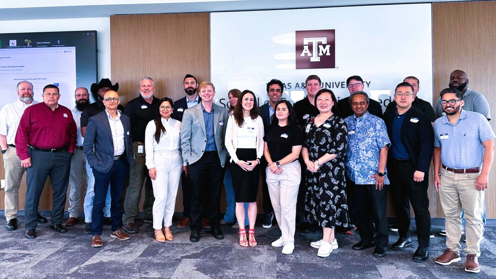 A large assembly standing in front of a Texas A&amp;M University sign. 