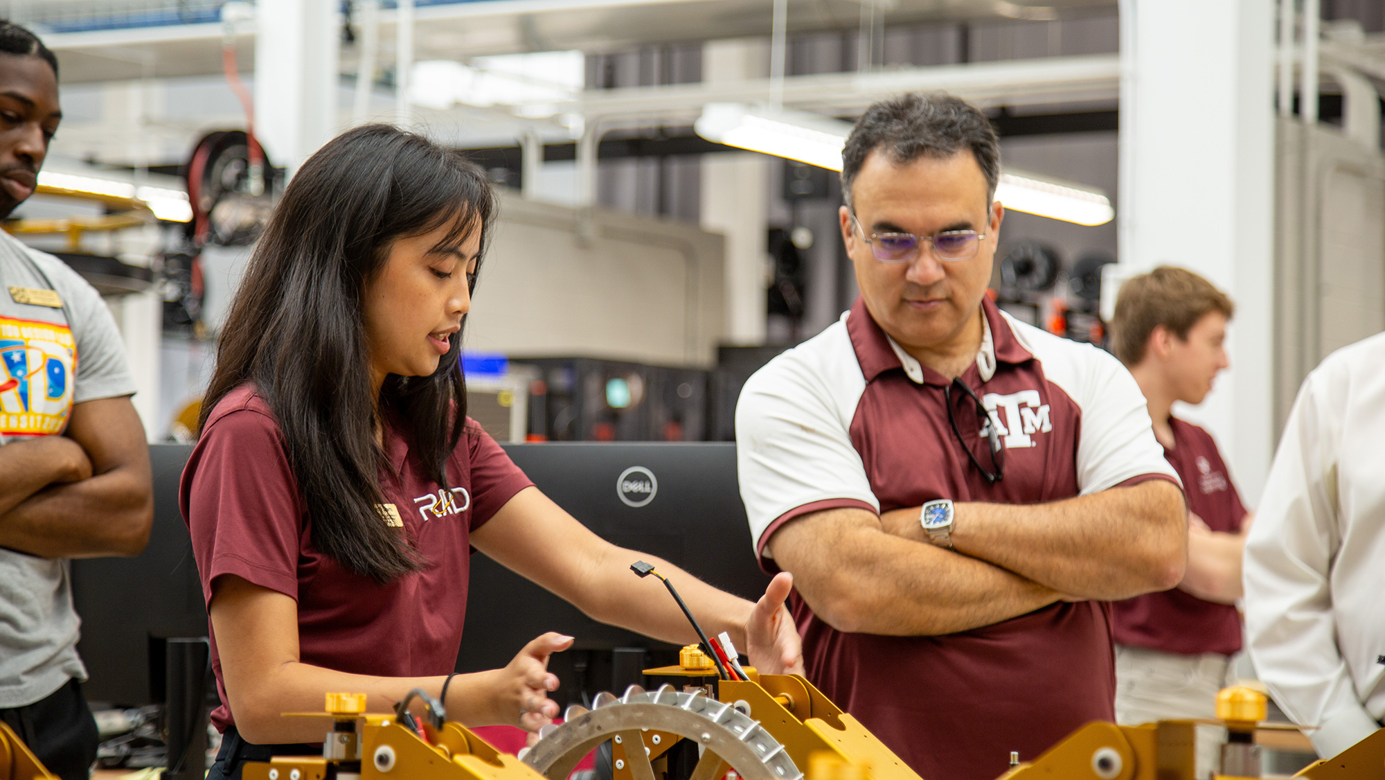 A woman and a man discussing a mechanical project in a workshop setting.