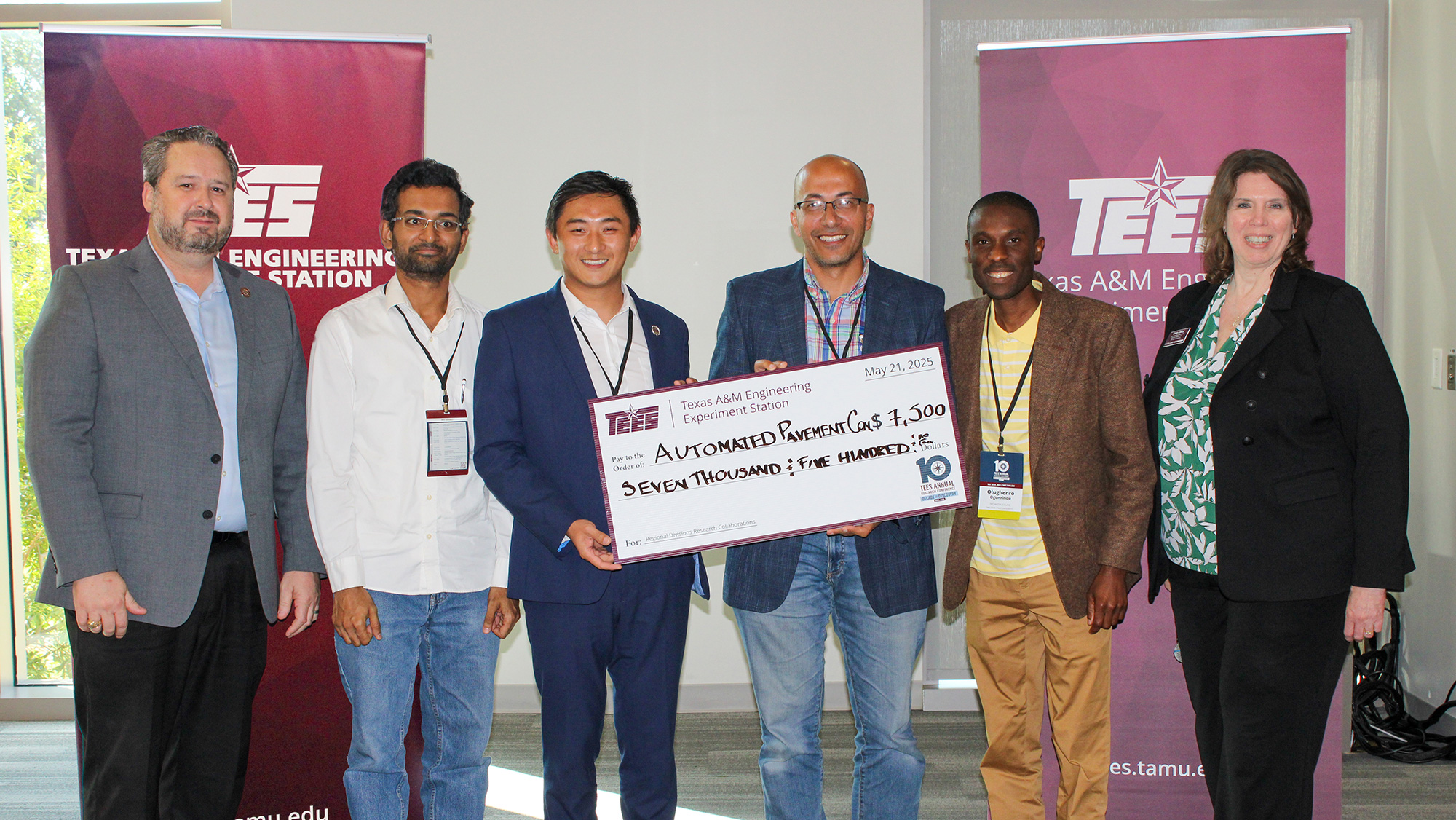 Six people stand in front of maroon banners holding a large check. 