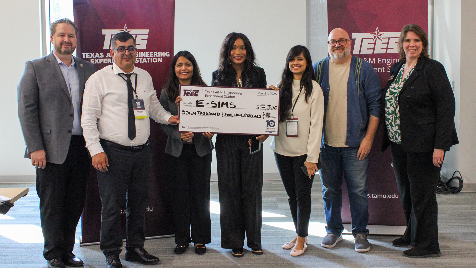 Seven people stand in front of maroon banners holding a large check. 