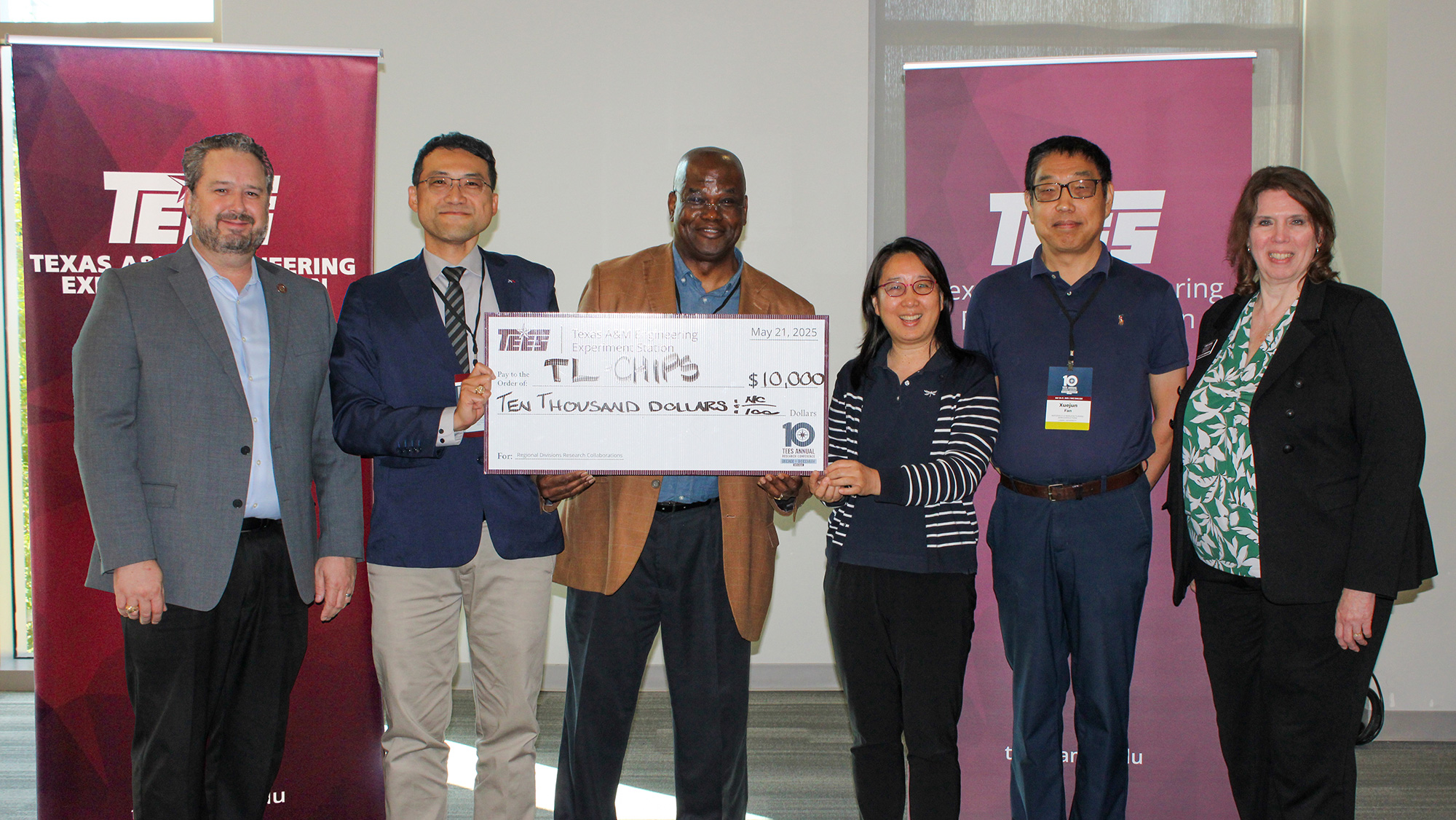 Six people stand in front of maroon banners holding a large check.
