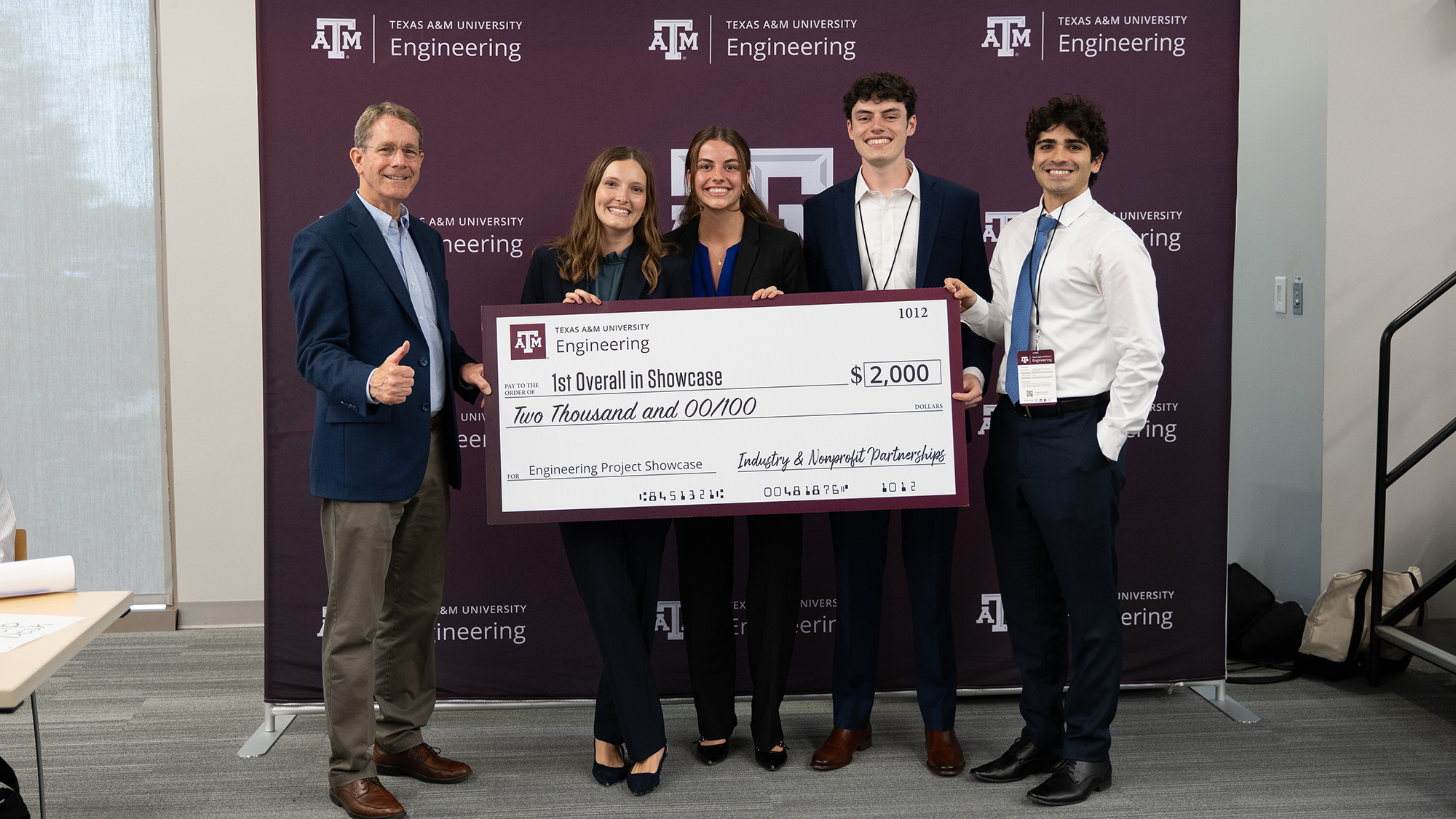 Three men and two women smile with large check.