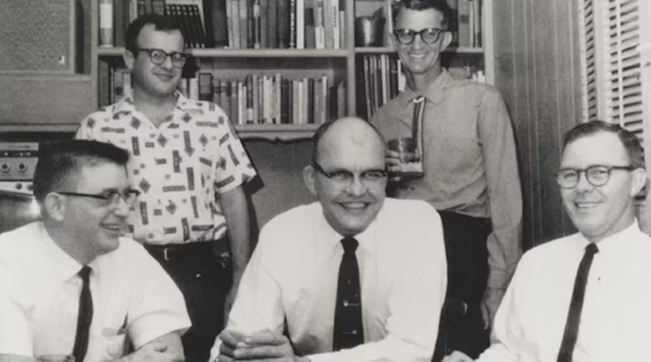 Two men standing and three men sitting, all smiling.