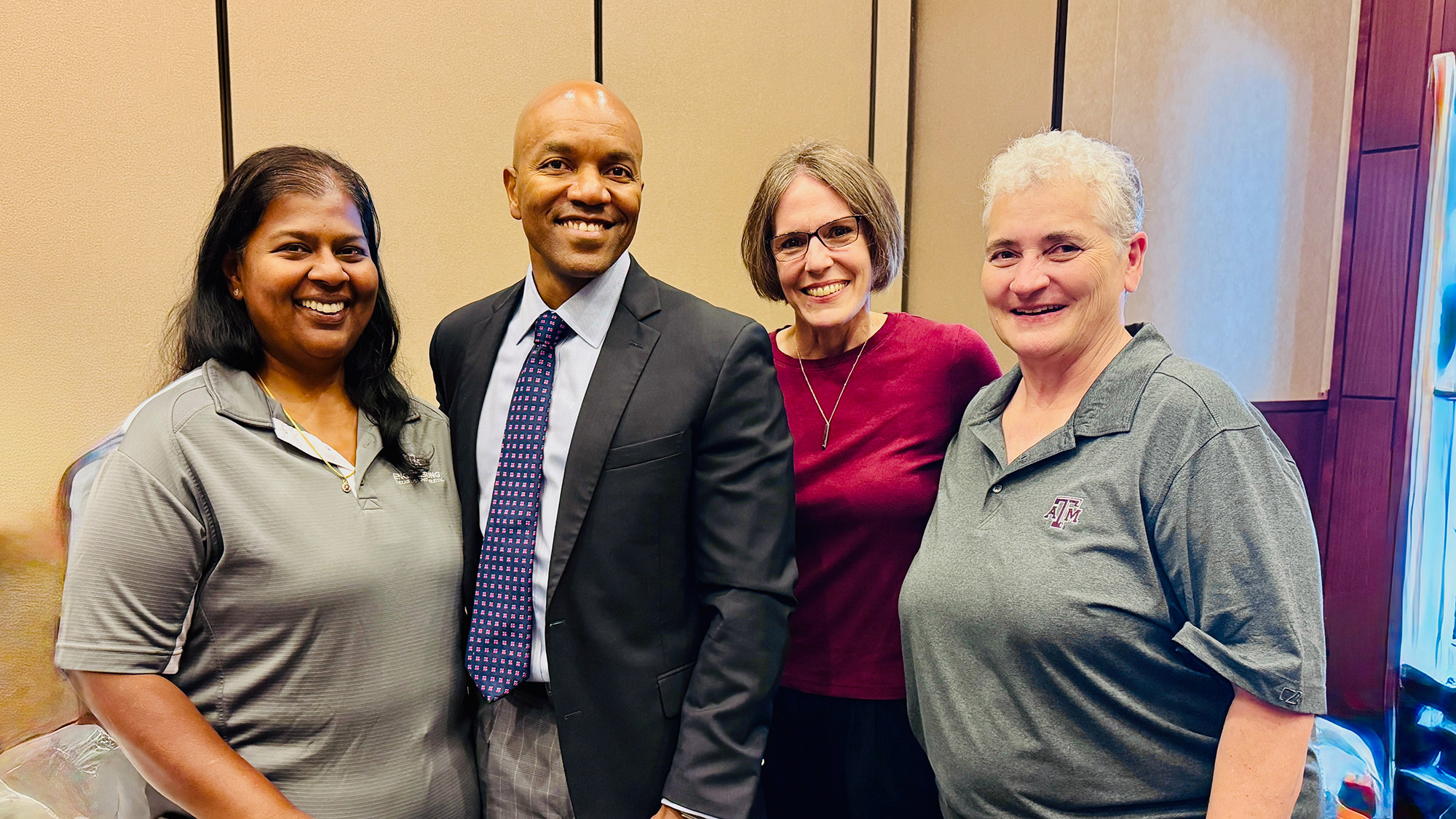 Four professionals pose for a group photo, smiling and standing together in a conference setting.