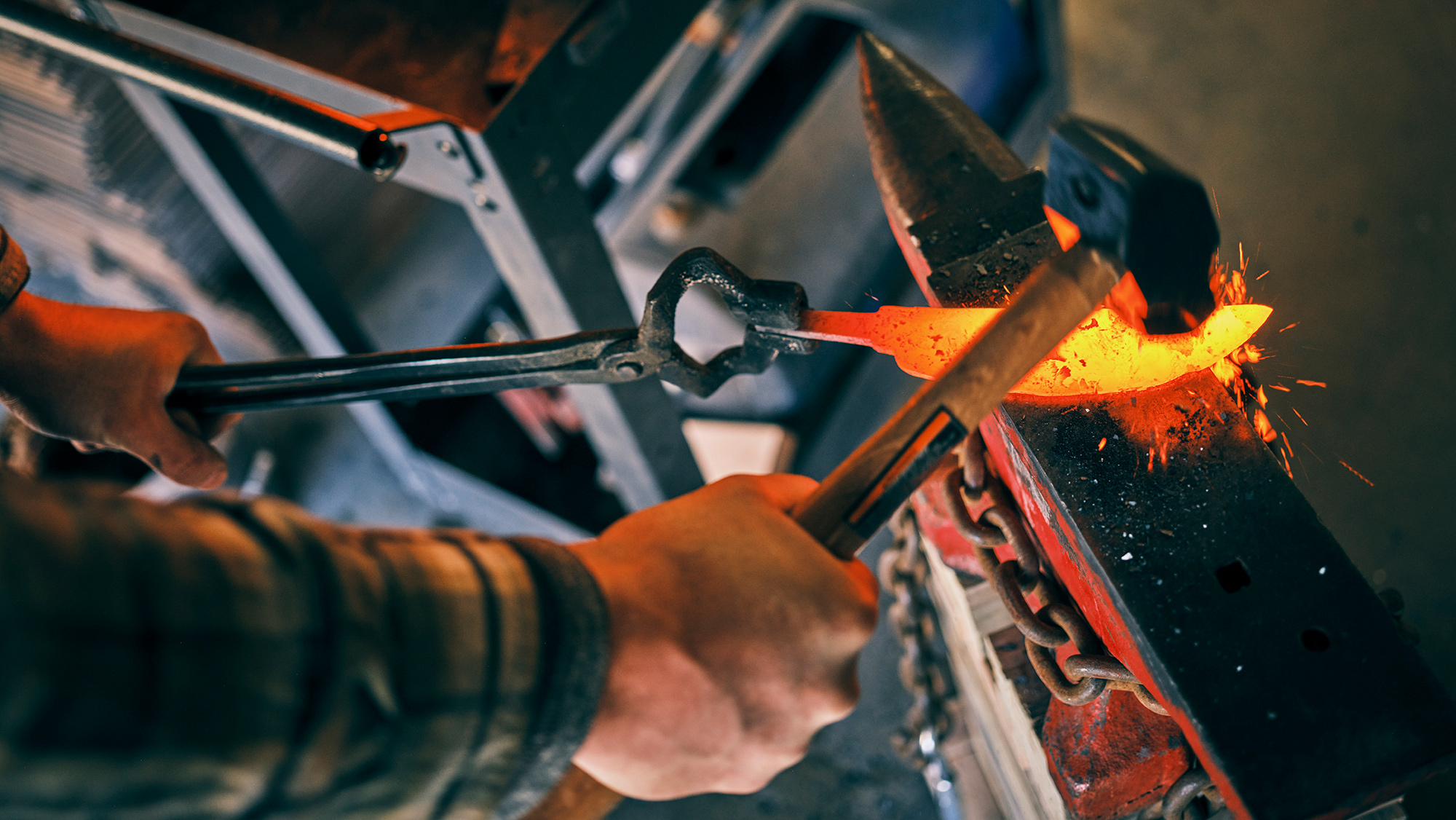 A blacksmith strikes a glowing piece of metal on an anvil with a hammer.
