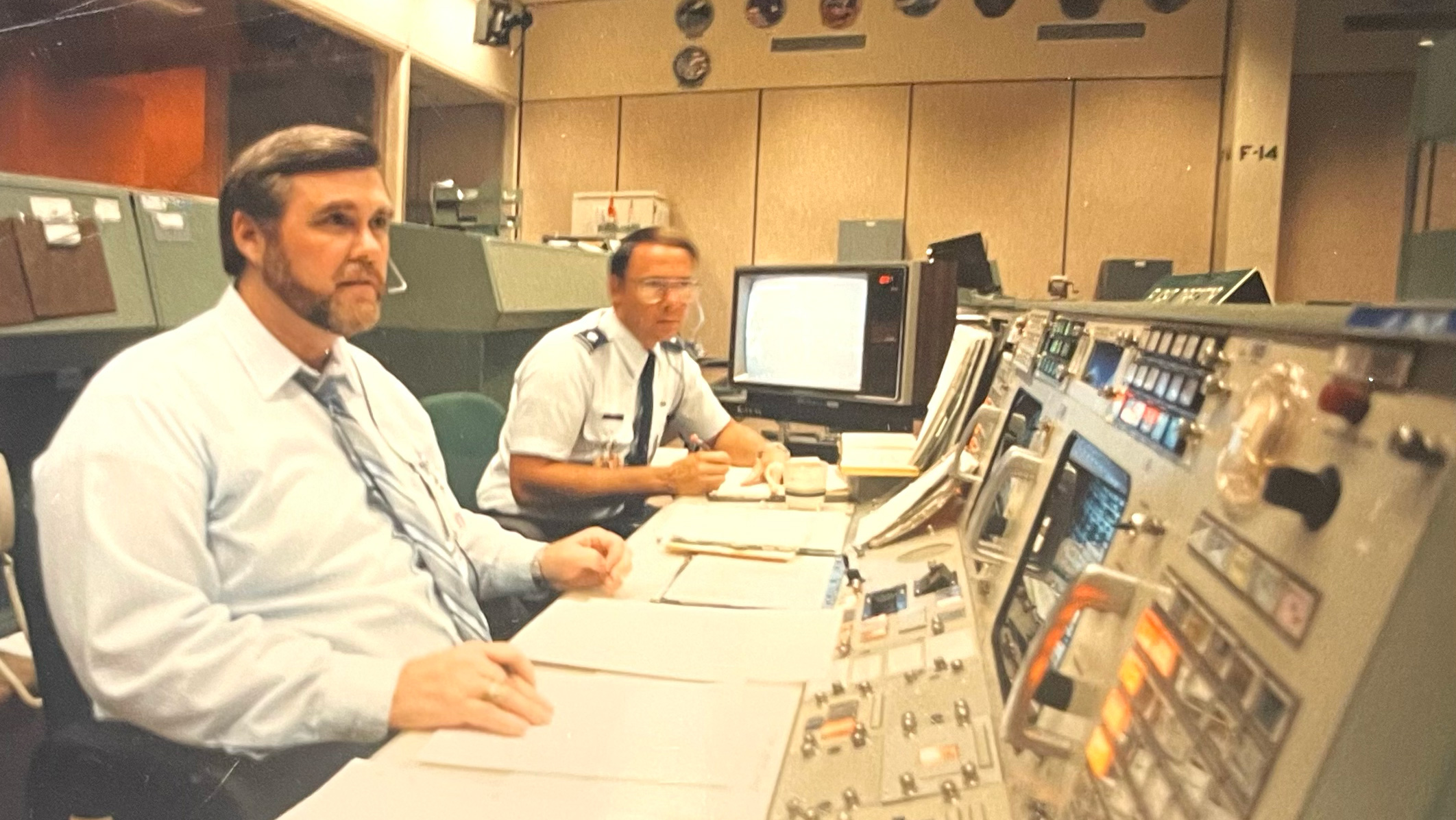 Two men sitting behind a mission control console.