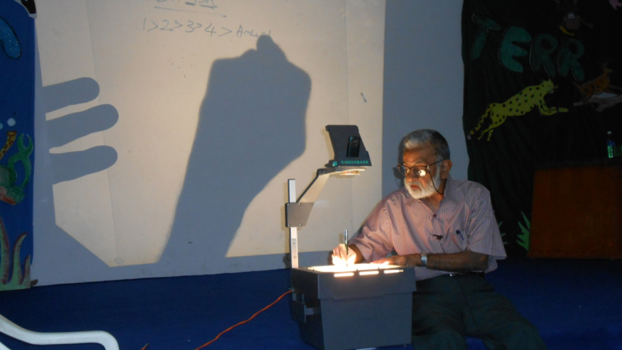 A man teaching at the front of a classroom. 