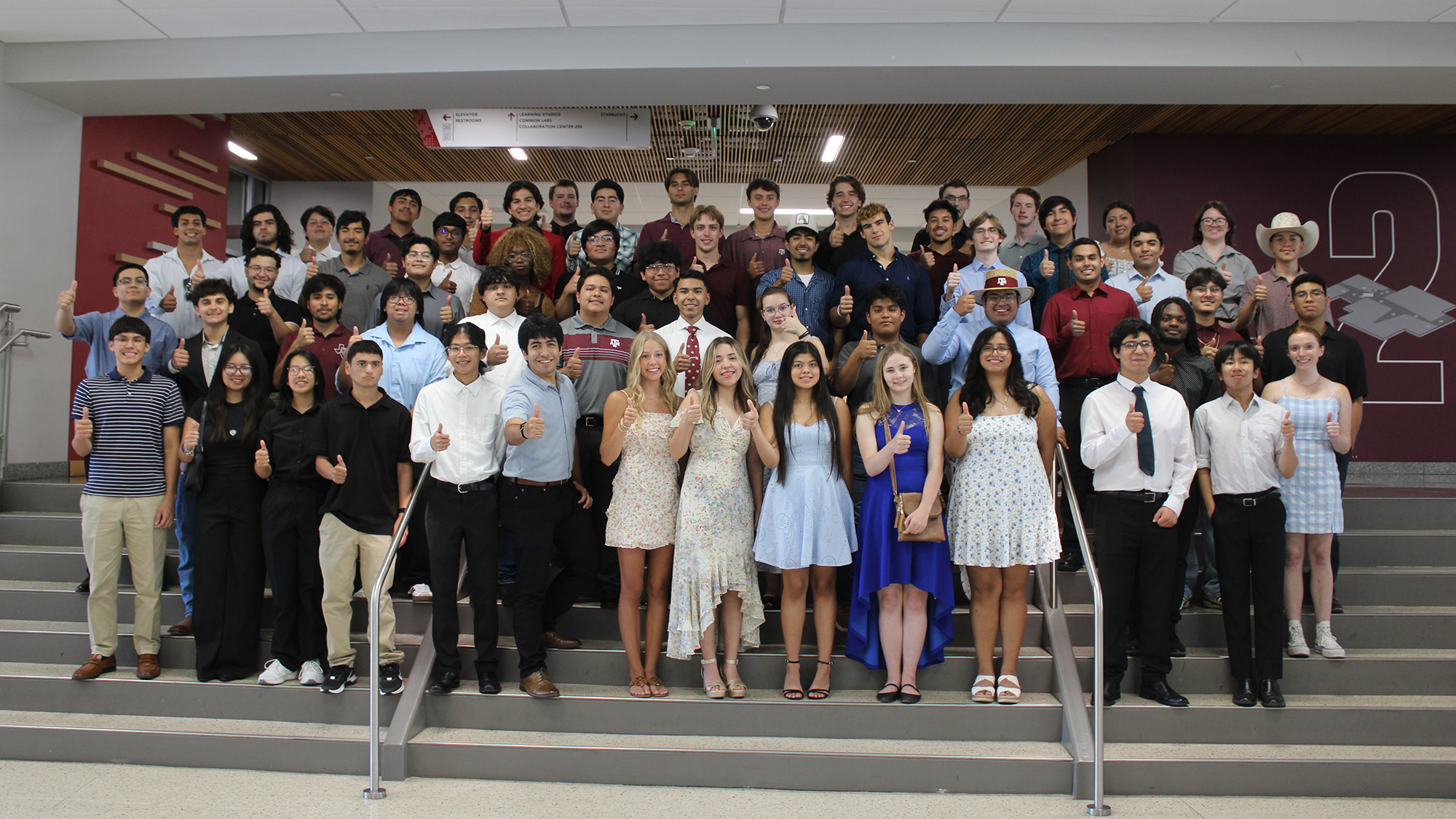 Summer Bridge Program participants stand on the stairs smiling and giving a thumbs up.