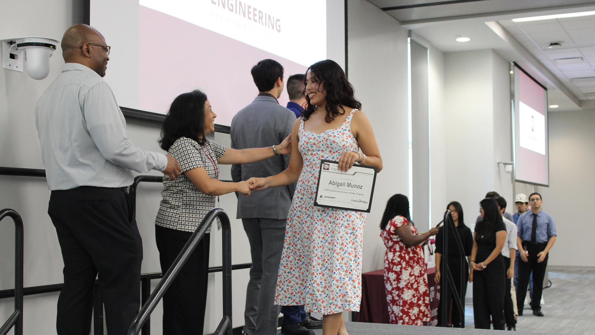 A group of students pose in front of a Texas A&amp;M Engineering backdrop while holding certificates.