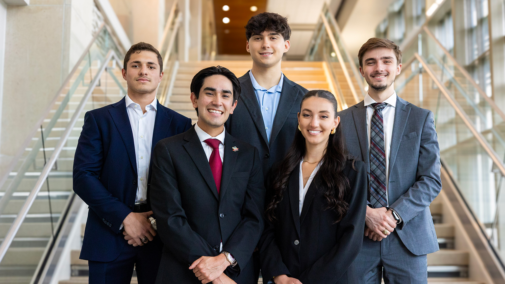 Five students dressed in professional attire on the steps of a campus building.