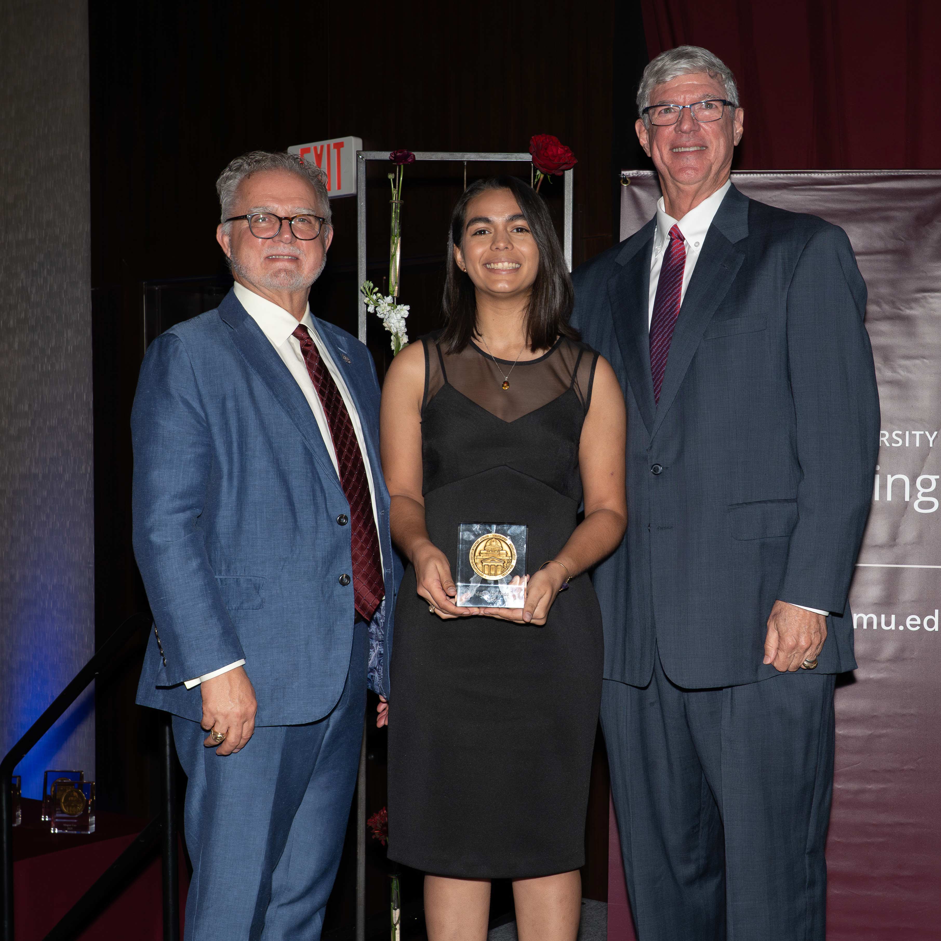 A woman and two men posing with an award.