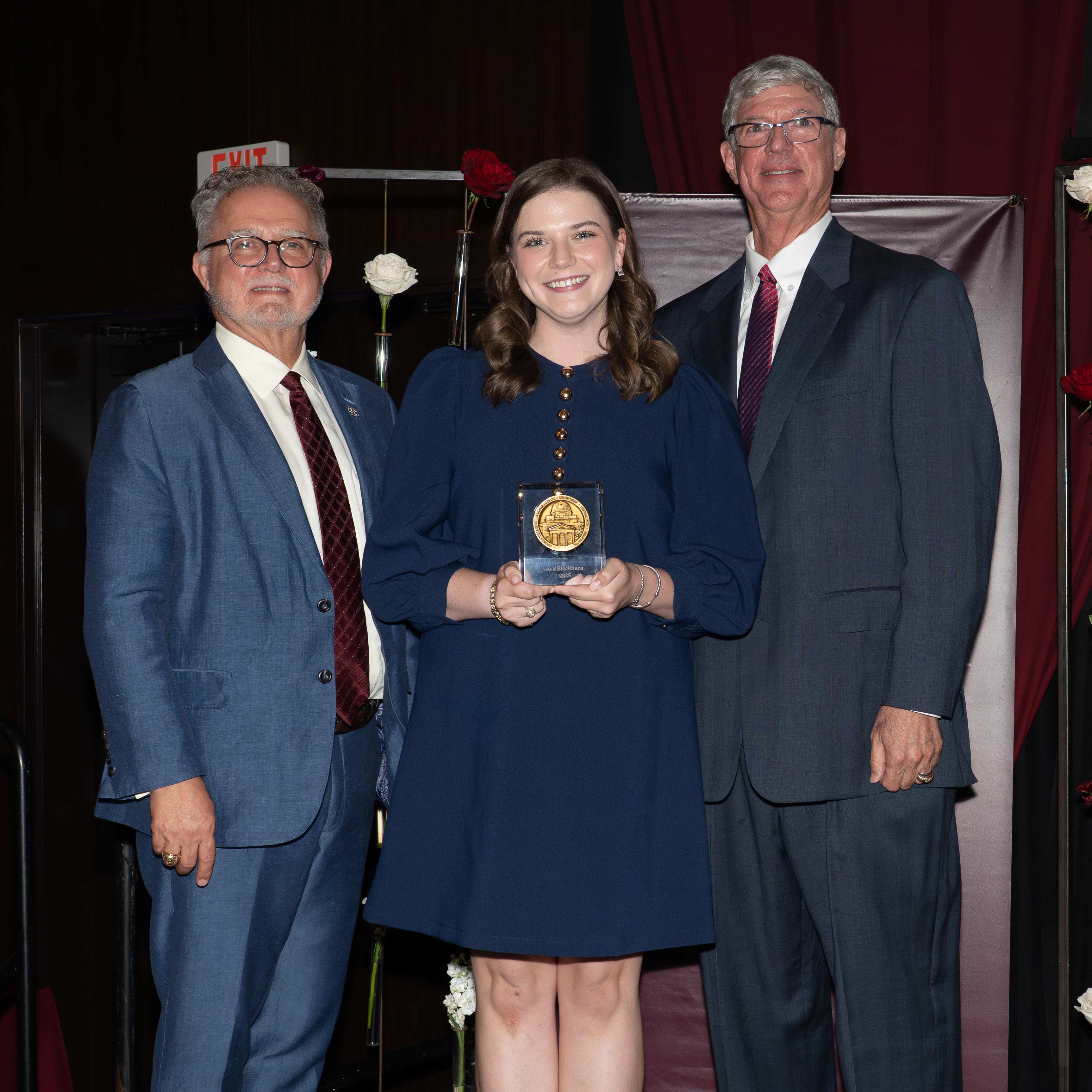 A woman and two men posing with an award.