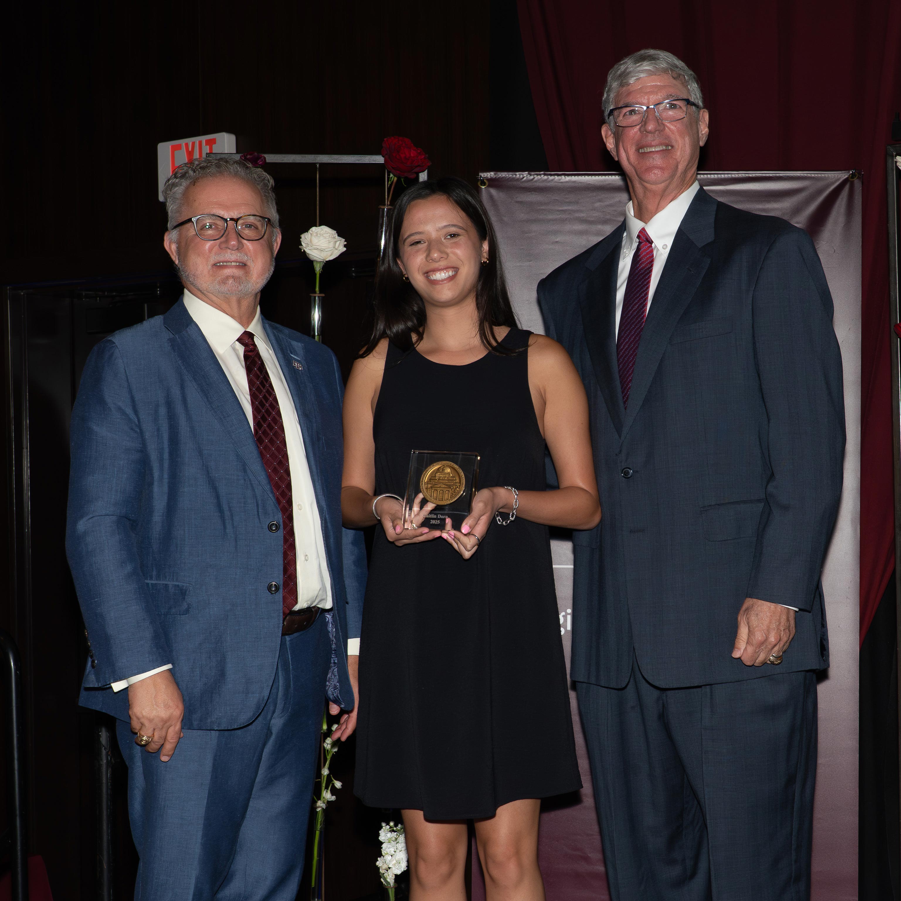 A woman and two men posing with an award.