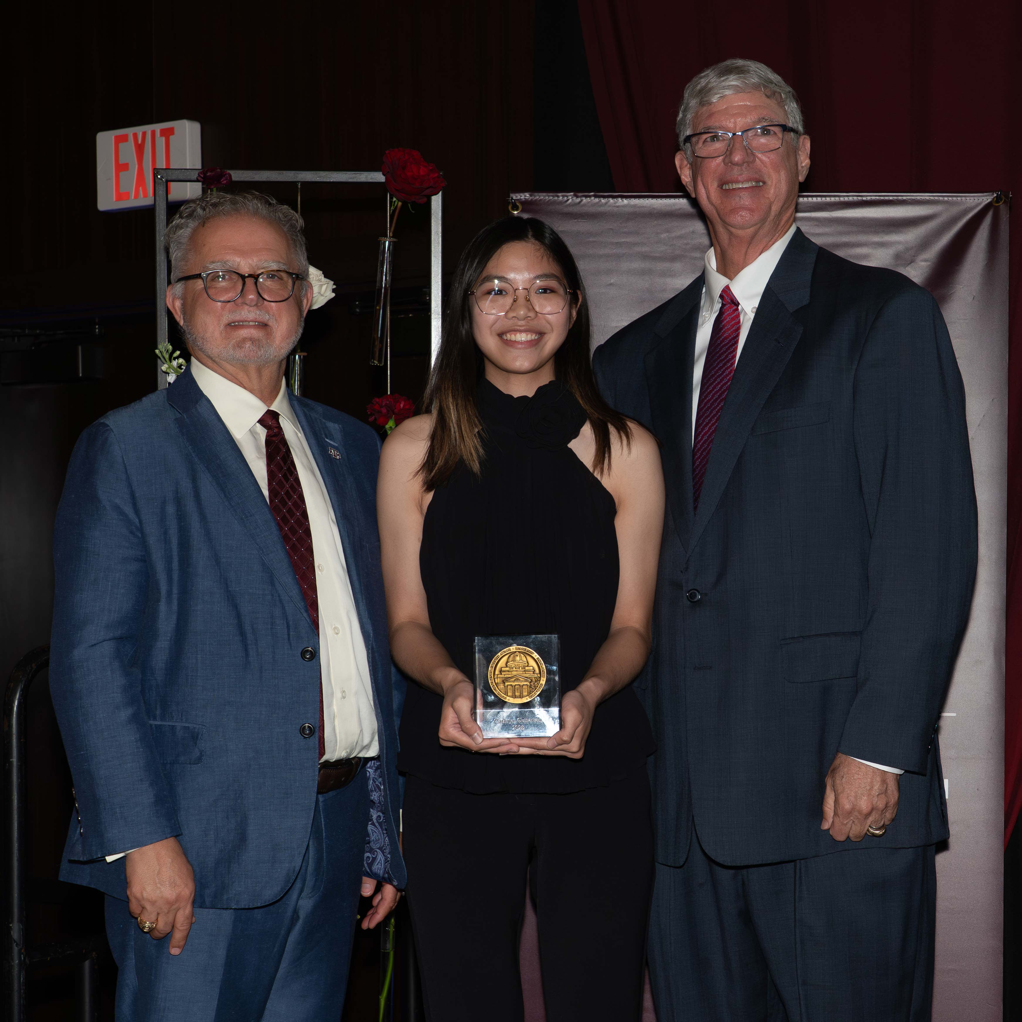 A woman and two men pose with an award.