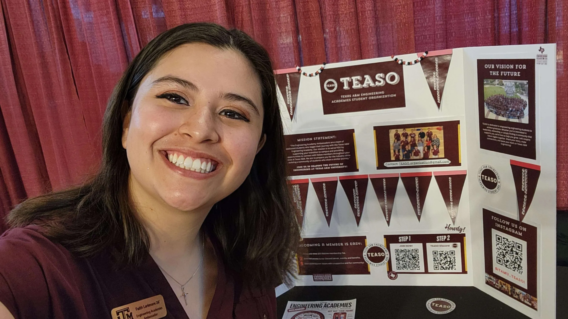 A woman wears a maroon blouse and smiles next to a Texas A&amp;M Engineering Academies Student Organization (TEASO) bifold at a Texas A&amp;M Engineering Academies Campus Engagement.