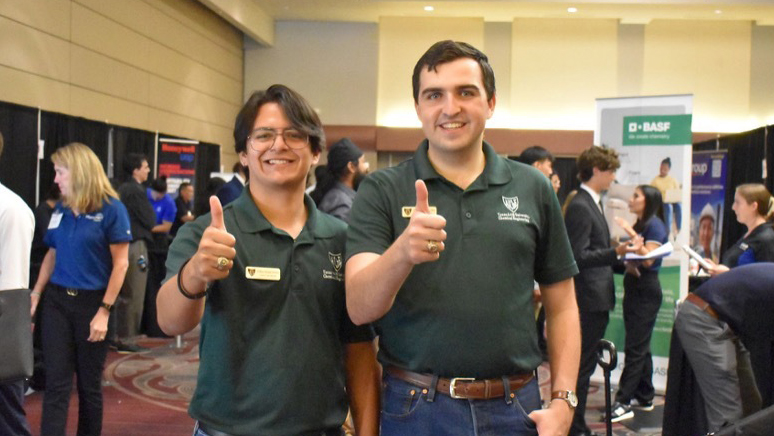 Two men smiling for a photo with their thumbs up.