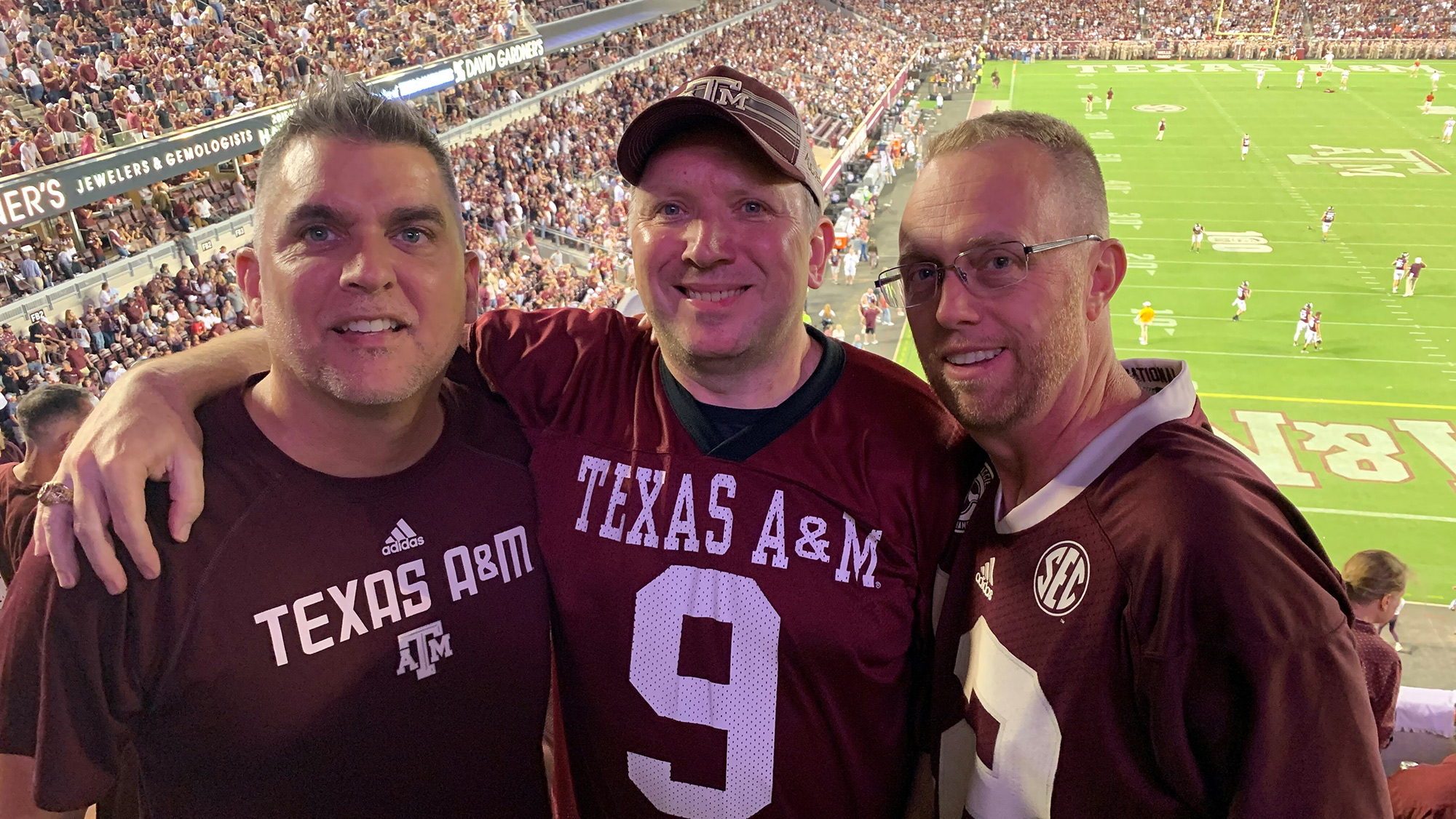 Three men standing with their arms around each other in front of a football field. 