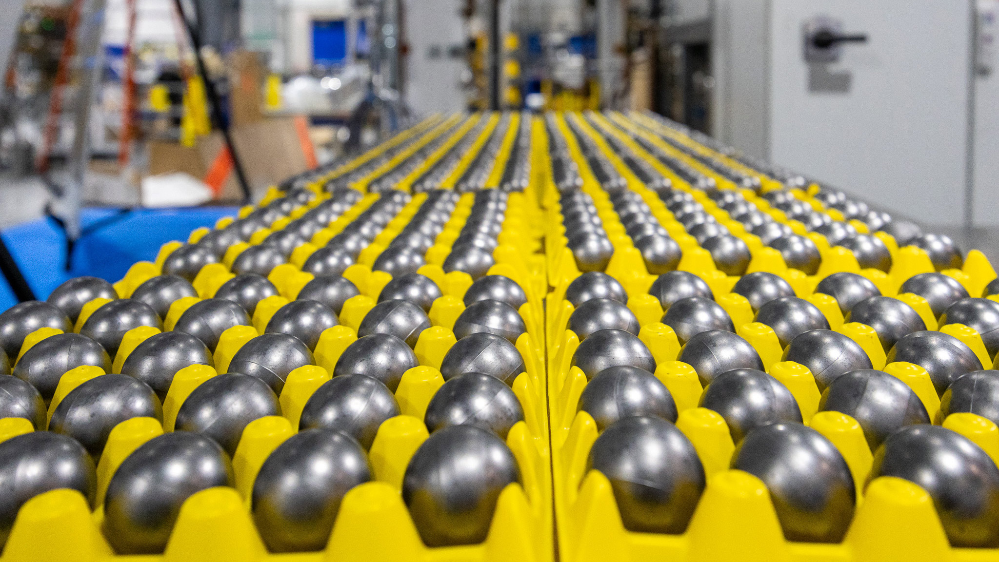 Rows of yellow industrial cylinders with metallic tops arranged inside a manufacturing facility.