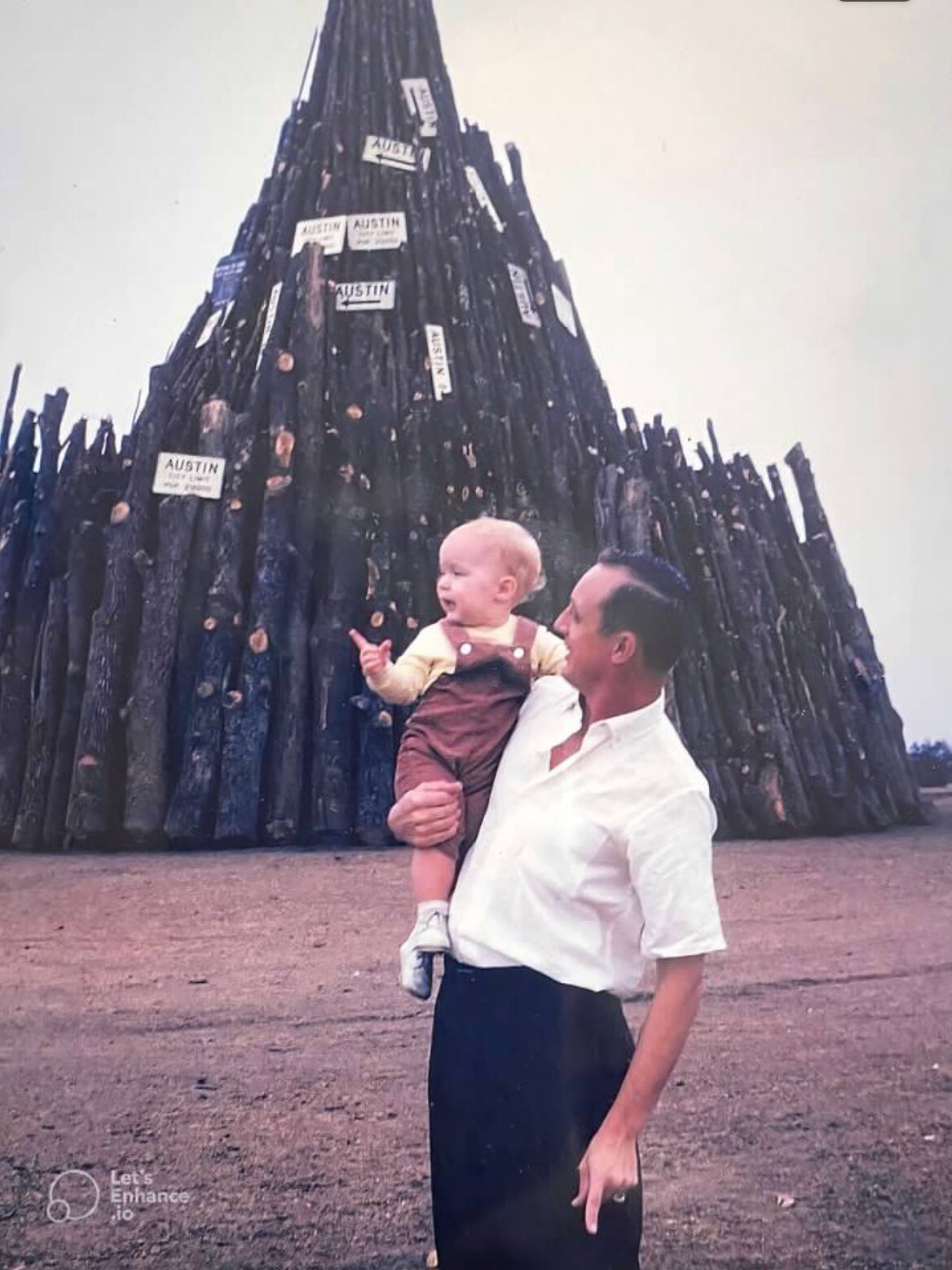 A man holding a baby next to a bonfire stack. 