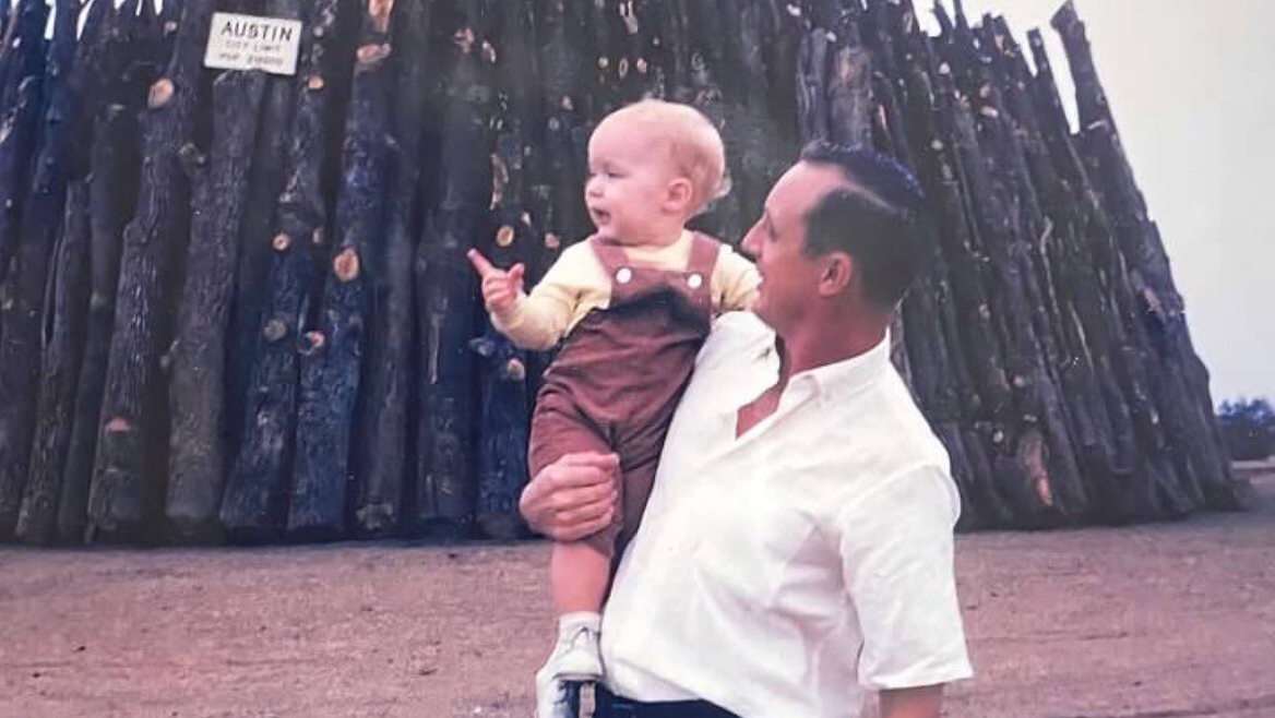 A man holding a baby next to a bonfire stack.