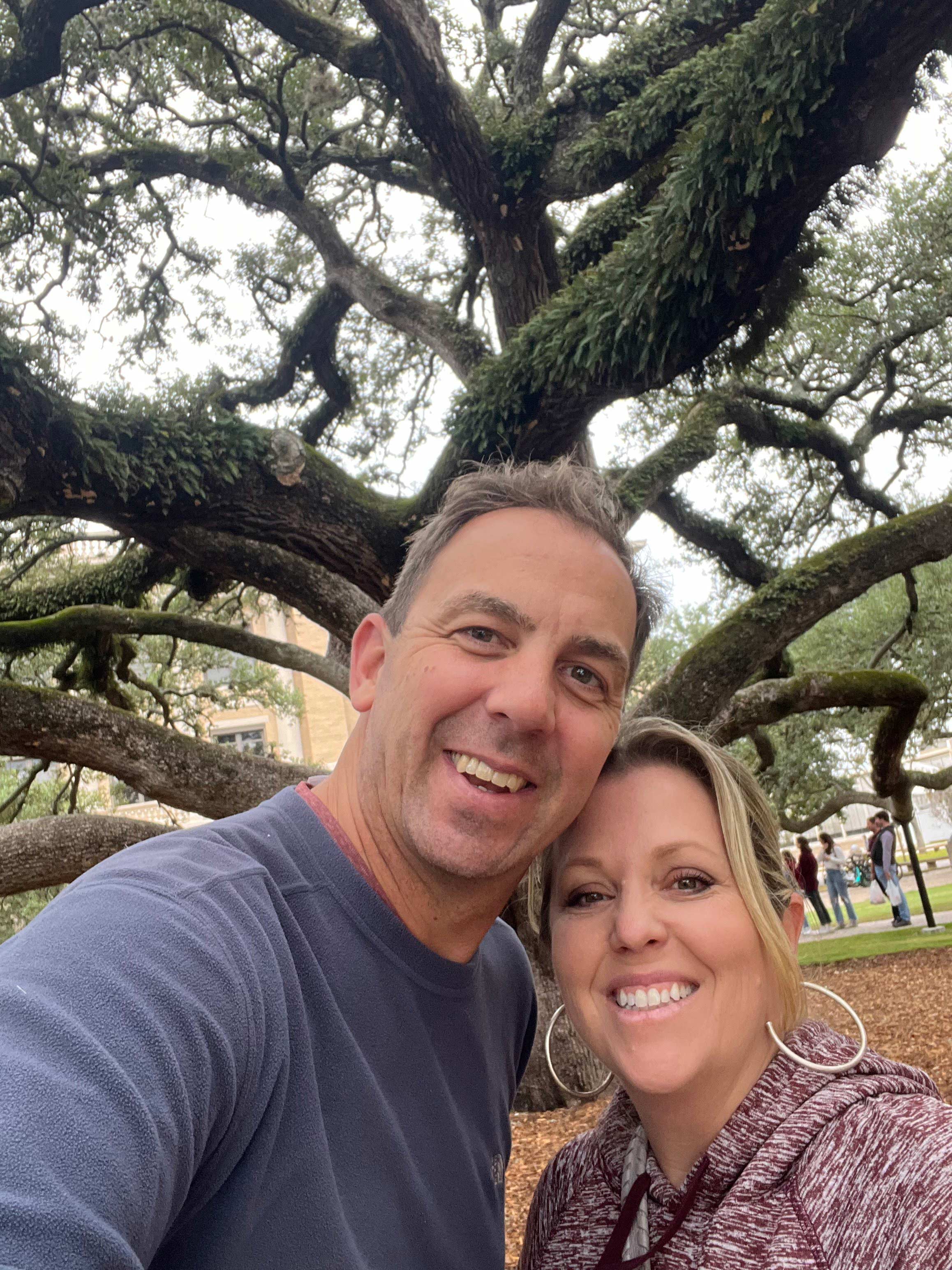 A couple taking a photo in front of a tree. 