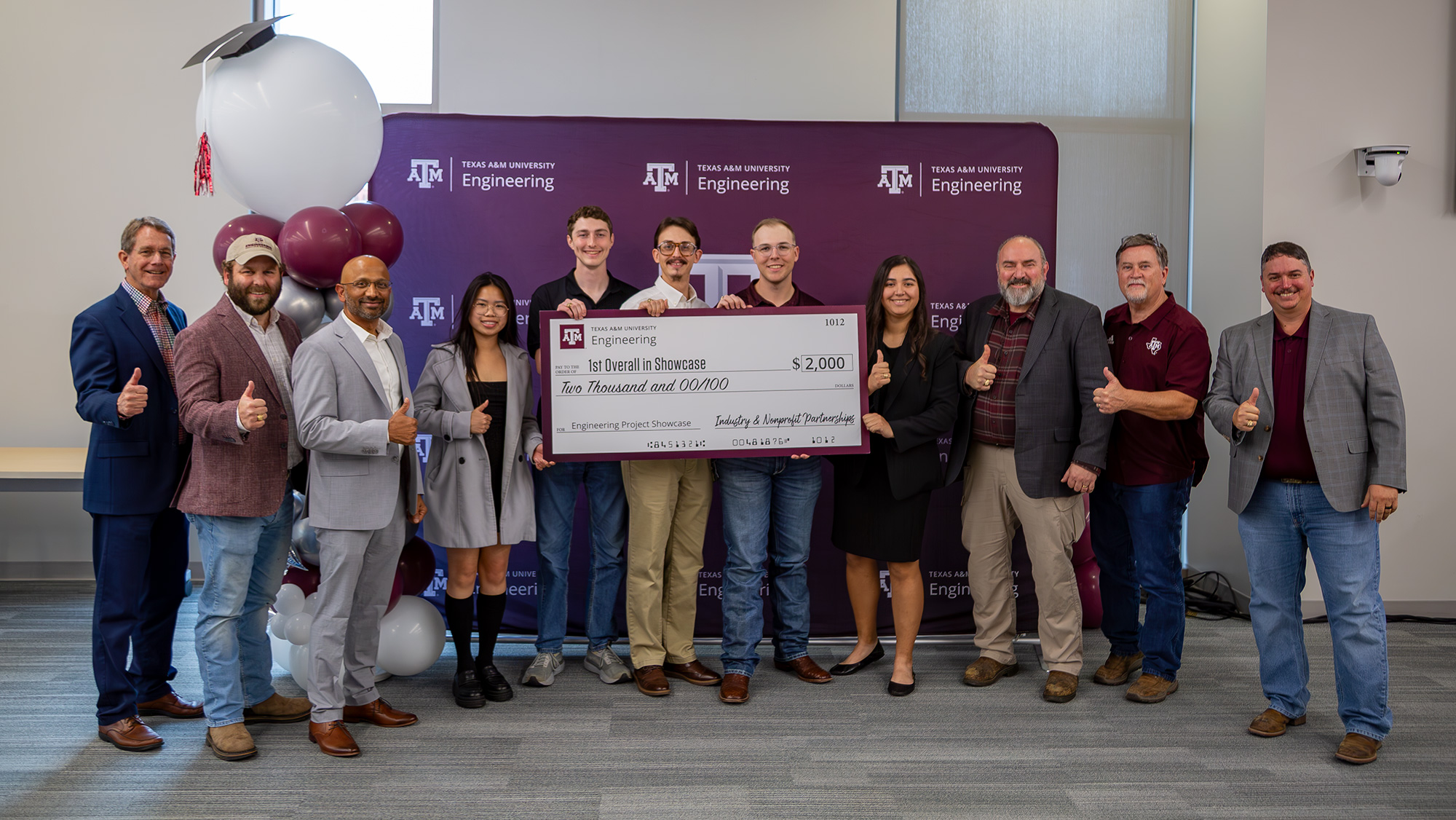 A group of students holding a jumbo check with professors on both sides of them.