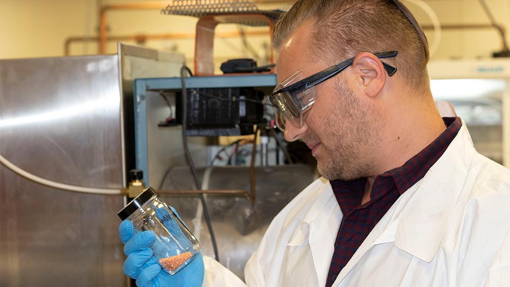 Scientist in lab coat and goggles holding a jar. 