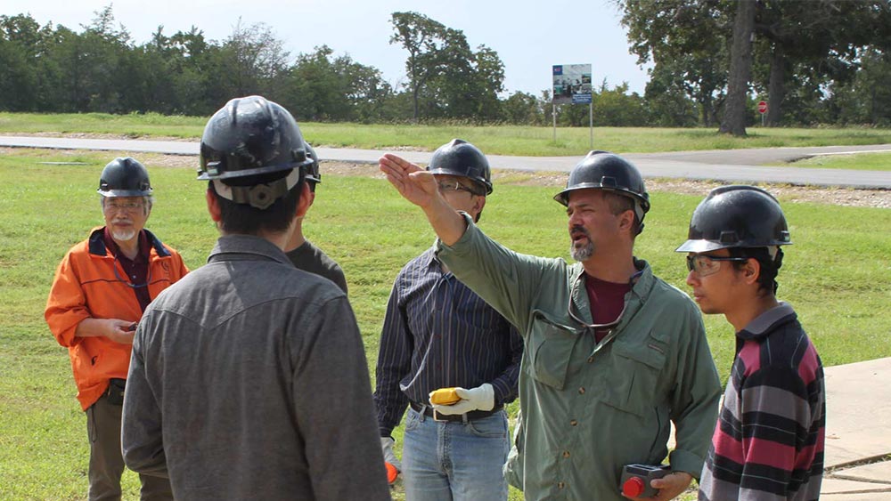 A group of workers on the sidewalk wearing hard hats. 