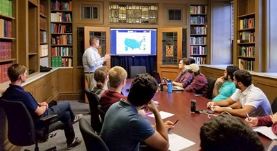 Group of students sitting around a large table looking at a presentation.