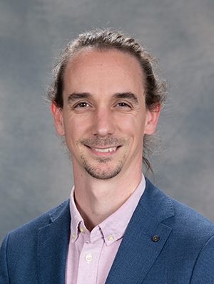 Carlo Fiorina wearing a blue crosshatch blazer and pink button-down shirt in front of grey background