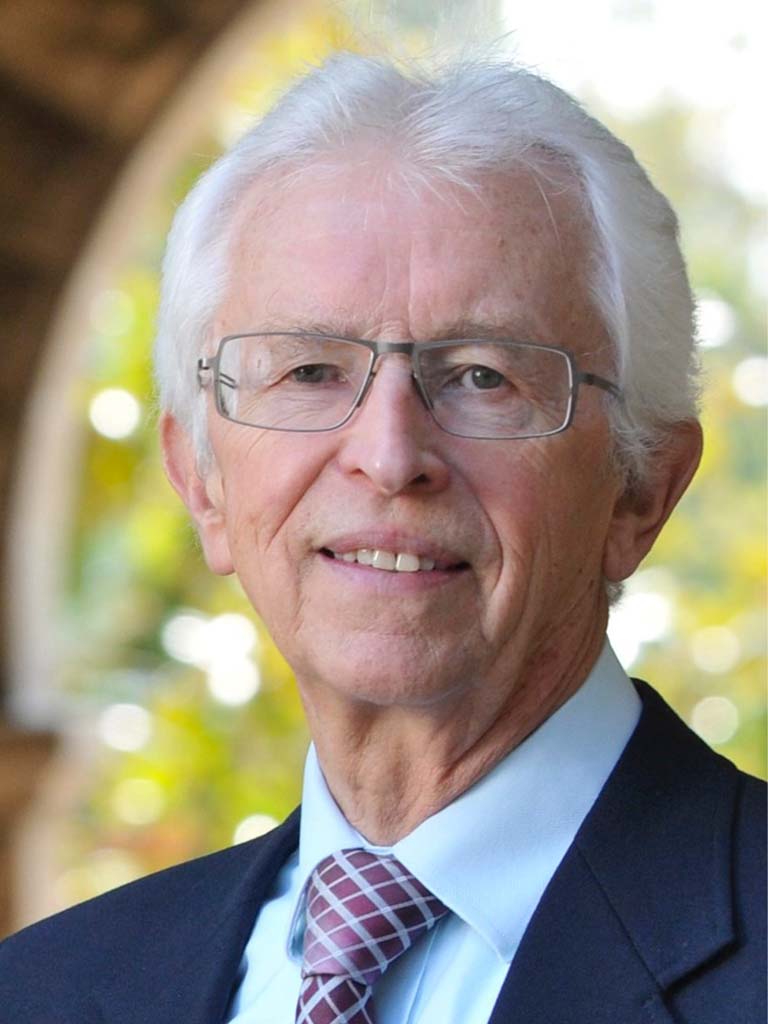 Dr. Seigfried Hecker wearing navy blue suit jacket with light blue shirt and maroon plaid tie. 