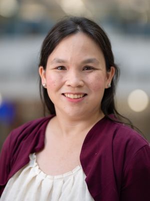 A smiling woman with long dark hair wearing earrings, a white blouse, and a maroon jacket.