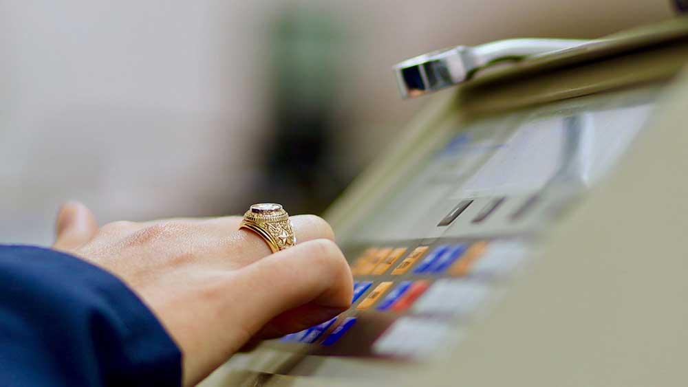 hand wearing Aggie ring pressing button on equipment control panel