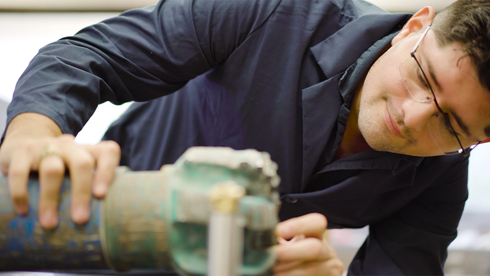 male graduate petroleum engineering student wearing lab coat while inspecting drill bit