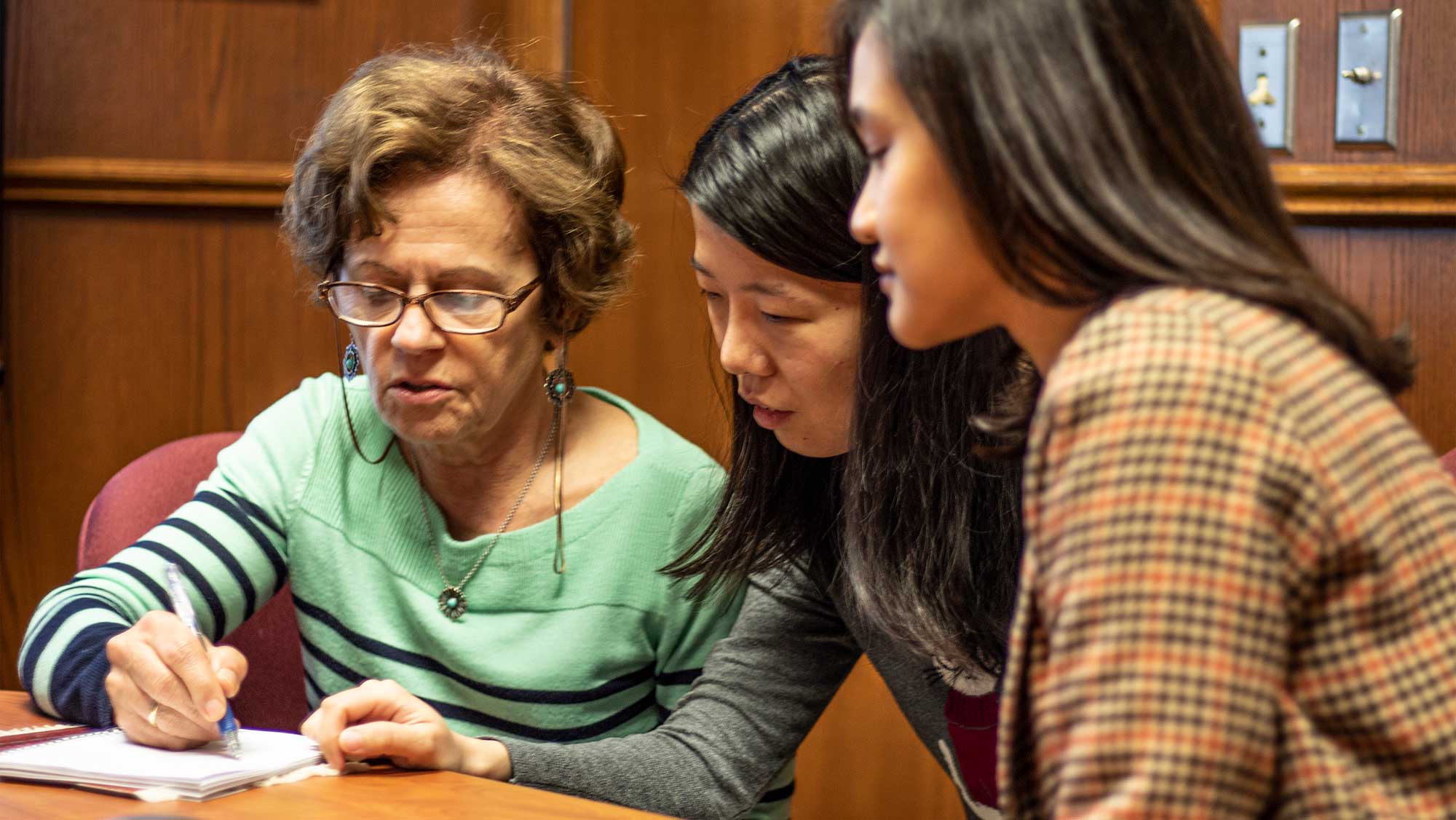 Female professor reviewing papers while seated at table with two female petroleum engineering students