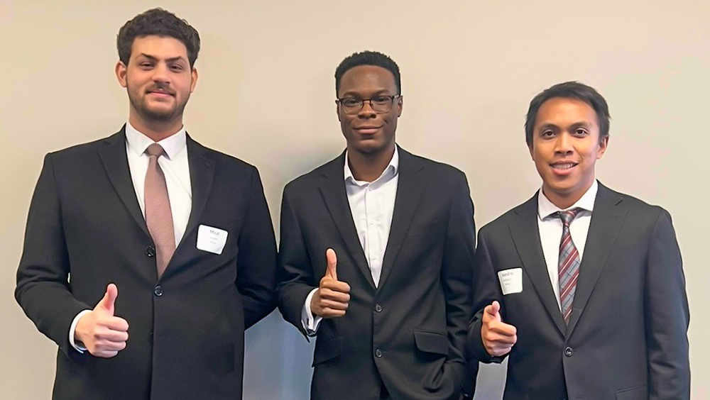 Three masters college students in business attire standing in a row and smiling.